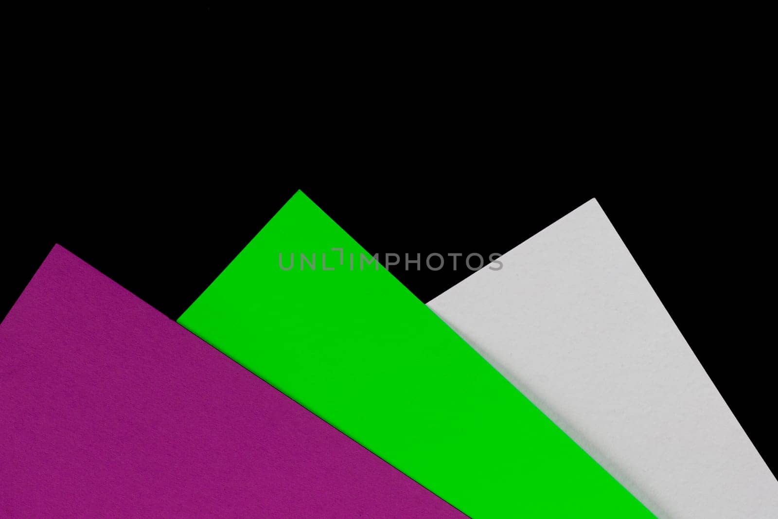 Part of purple, green and white colored paper on a black background. Geometric background from multi-colored cardboard.