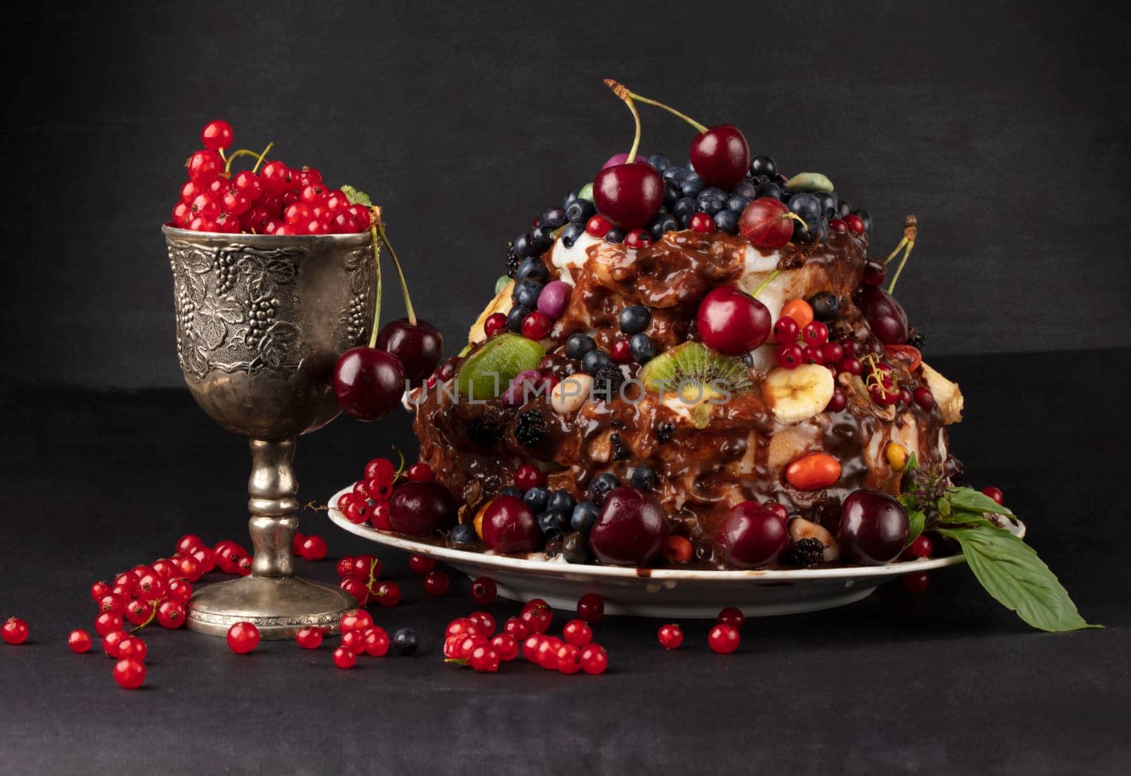 A luxurious cake with fruits and berries in a glass goblet on a dark background.