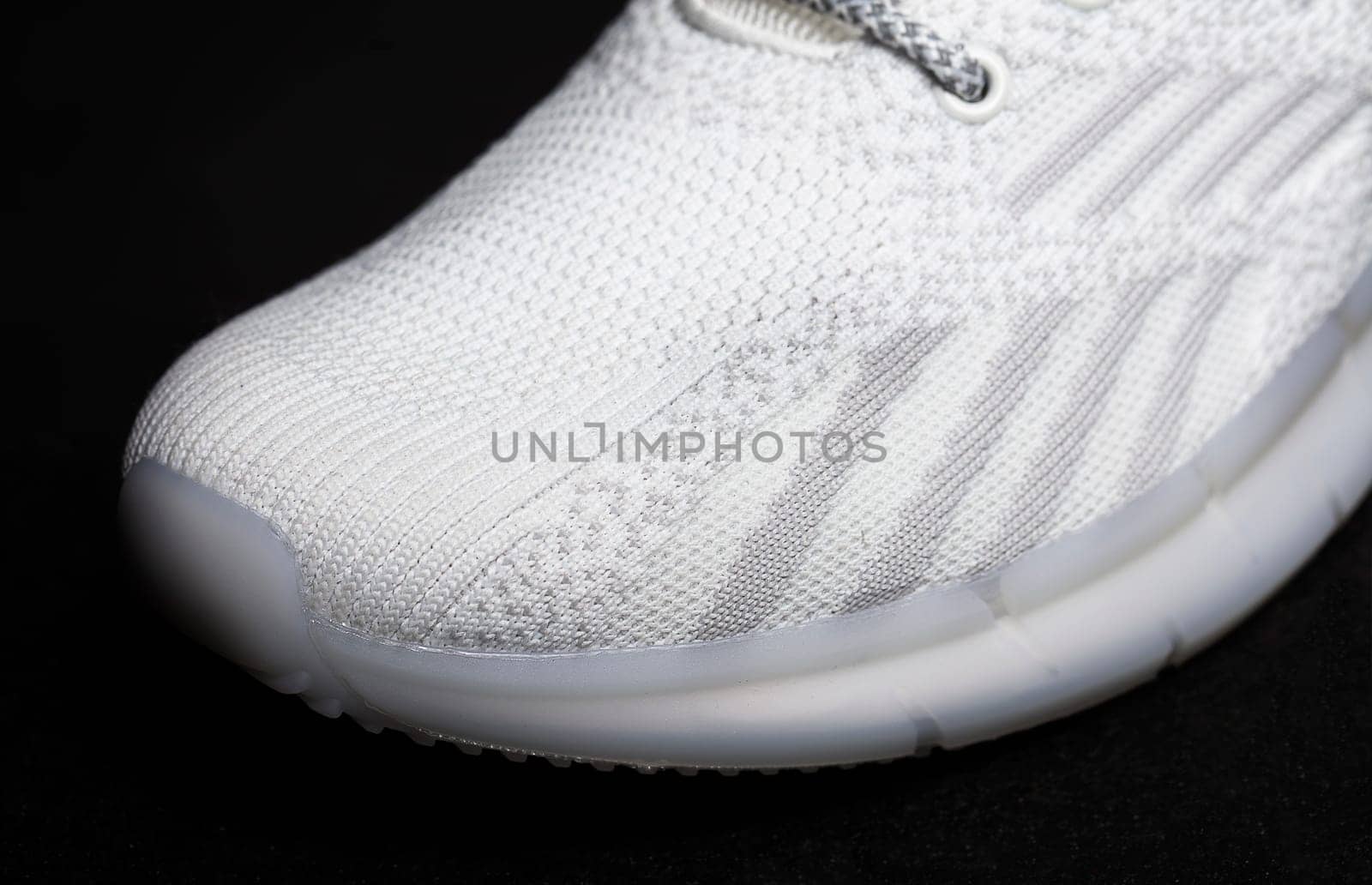 White fabric sneaker with embossed sole on a black background close-up.