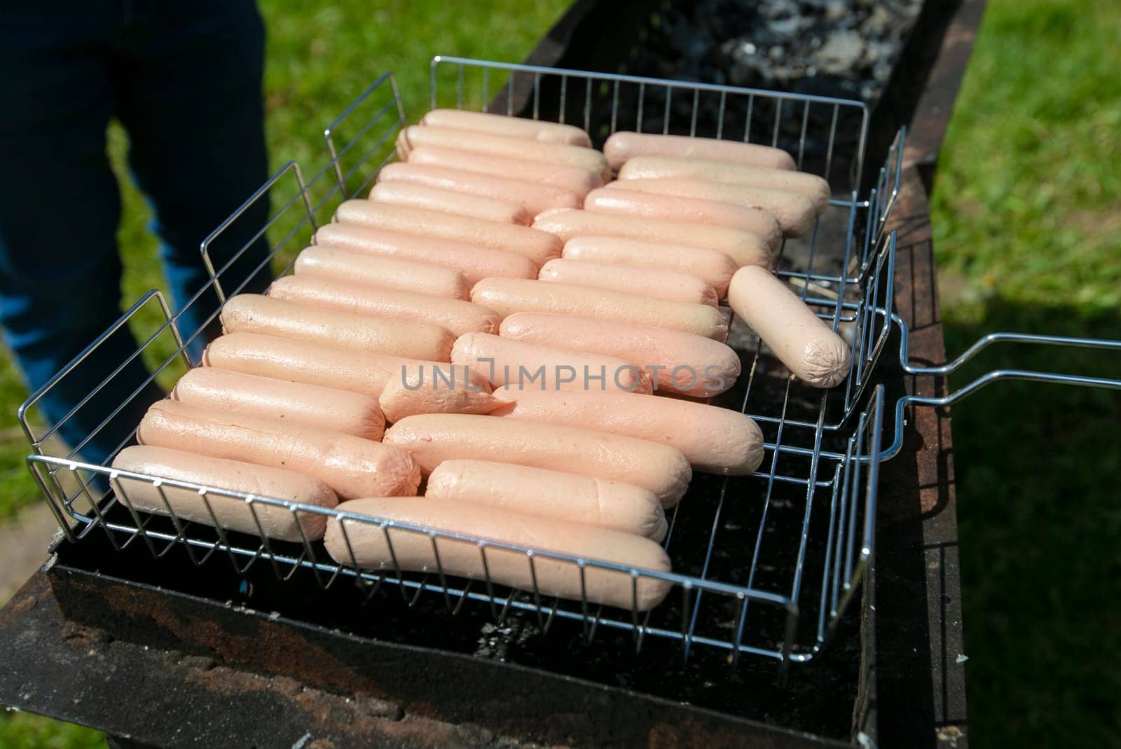 A lot of sausages are grilled on a barbecue grill for a buffet table. by Sviatlana