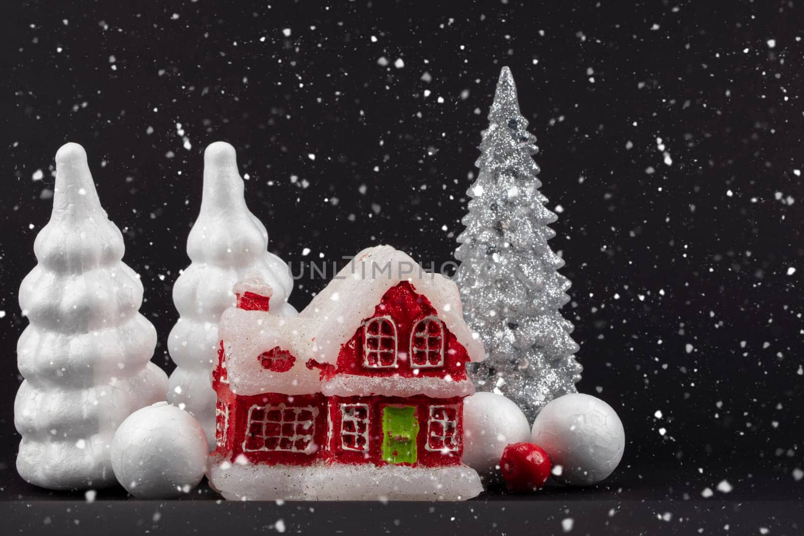 Festive snowy dark Christmas background. Red miniature house surrounded by white Christmas trees. by Sviatlana