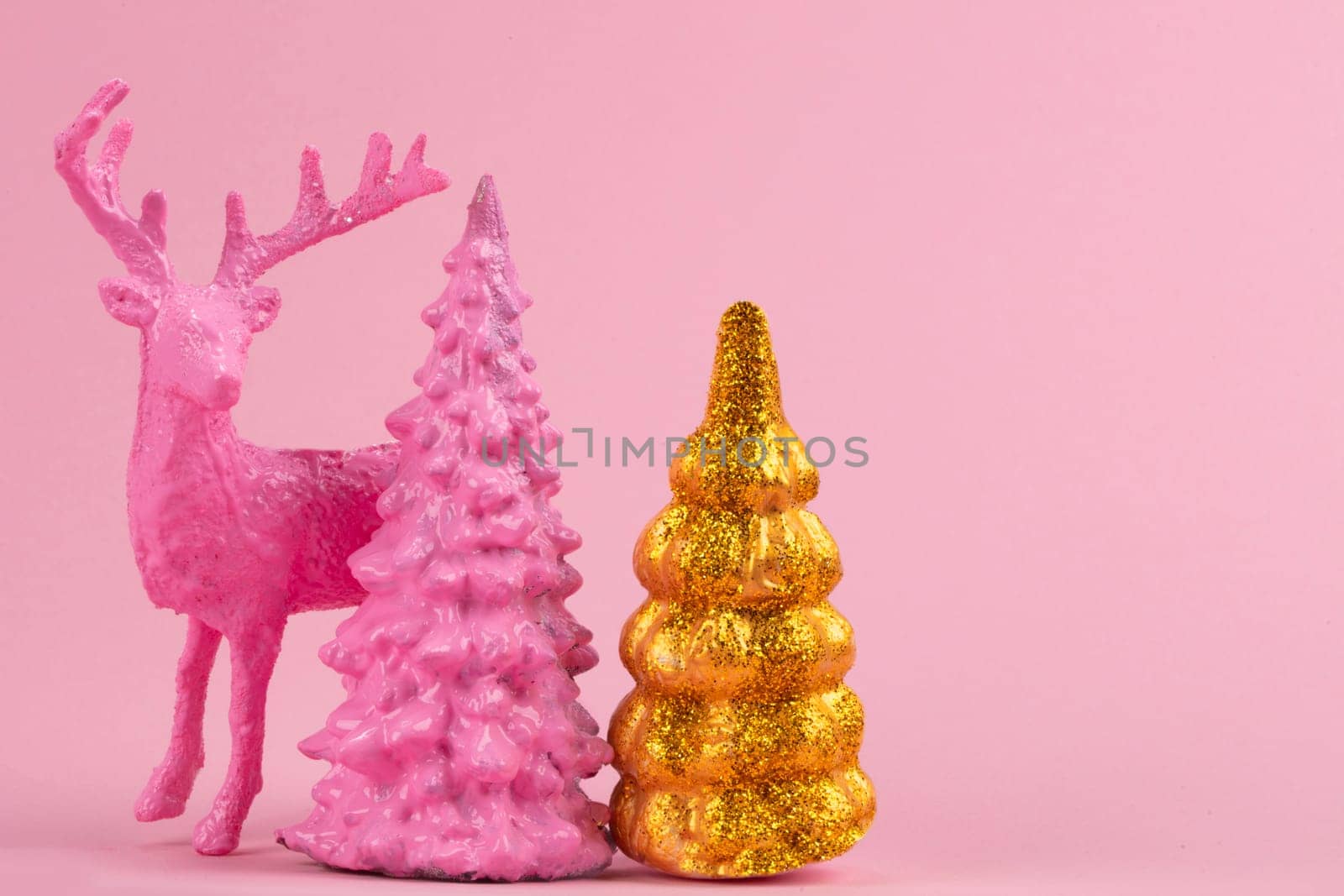 Festive Christmas background. Pink deer near miniature pink and gold Christmas trees.