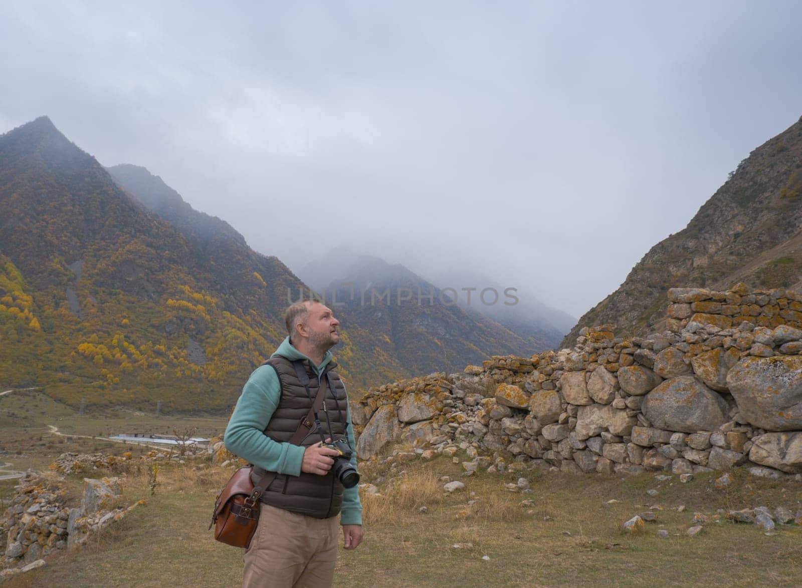 A male tourist takes pictures of a beautiful autumn mountain foggy landscape using a camera