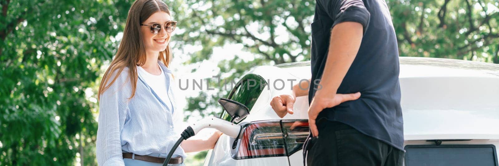 Focused EV car recharging electricity for battery on blurred couple. Exalt by biancoblue