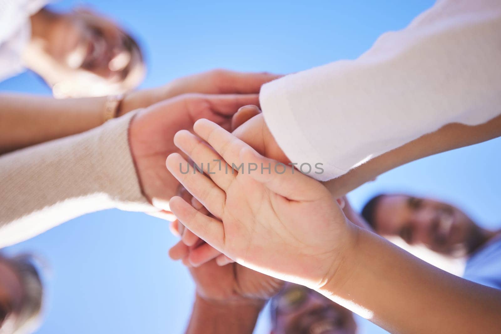 People, hands together and teamwork below in support for trust, bonding or unity and collaboration outdoors. Low angle of family or friends piling hand for team building, community or goals outside.