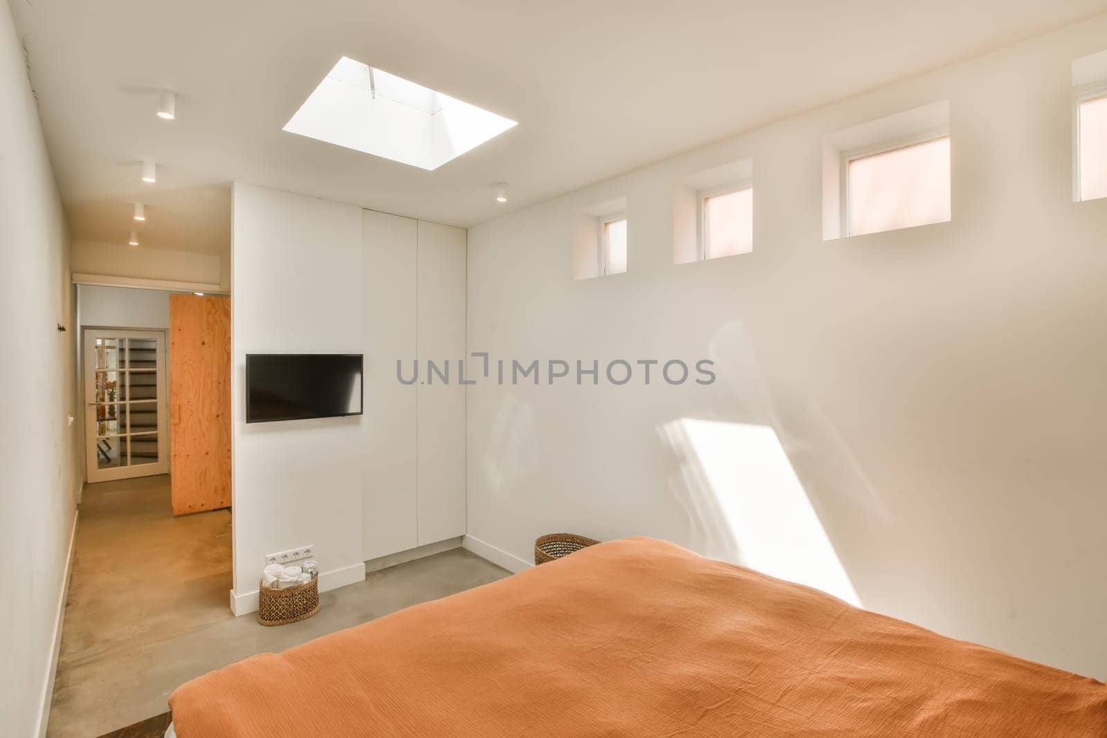a bedroom with an orange comforter on the bed and a flat screen tv mounted in the corner of the room