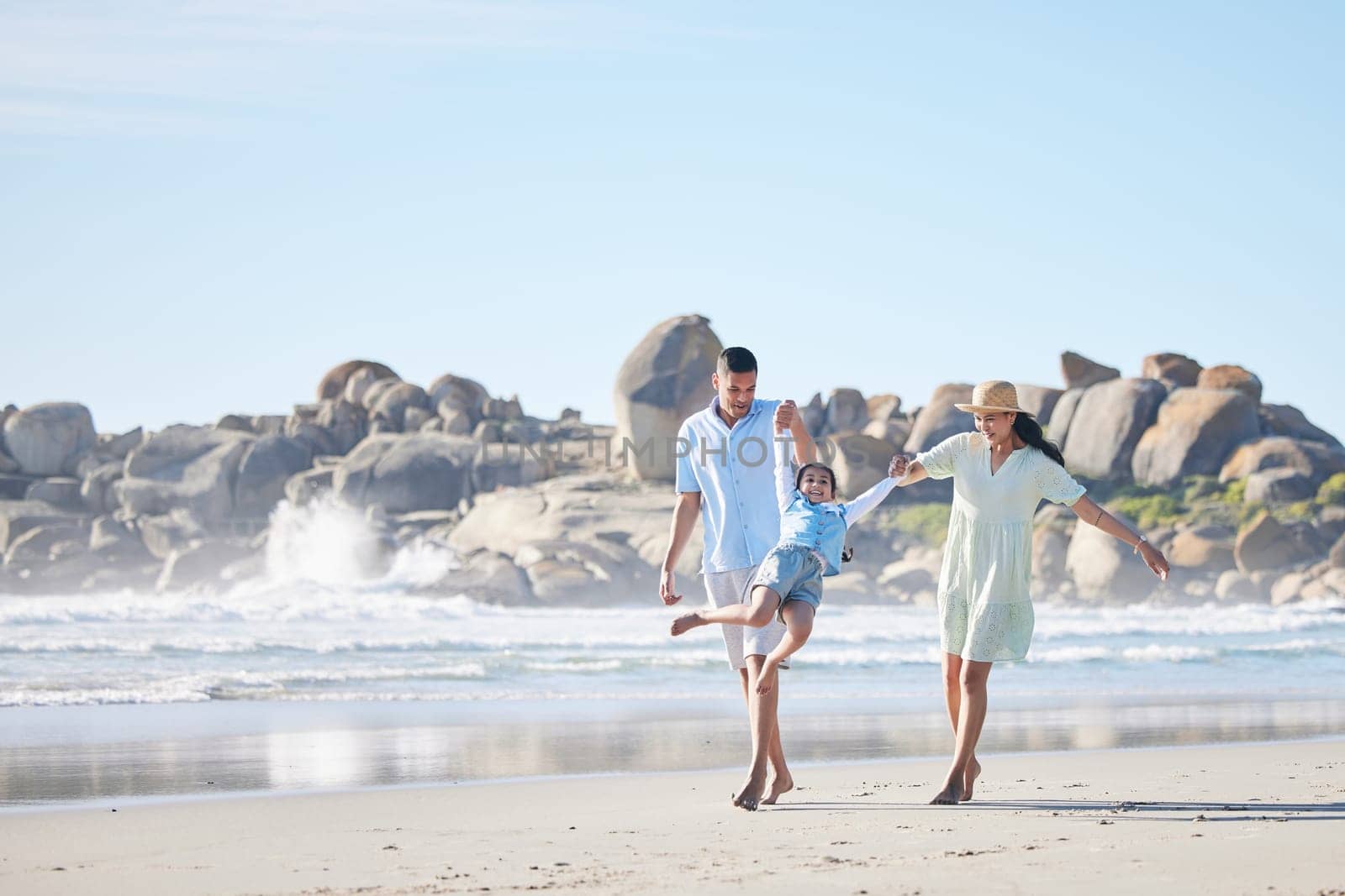 Family, parents and swinging a child at the beach for fun, adventure and play on holiday. A happy woman, man and young kid walking on sand and holding hands on vacation at ocean, nature or outdoor.