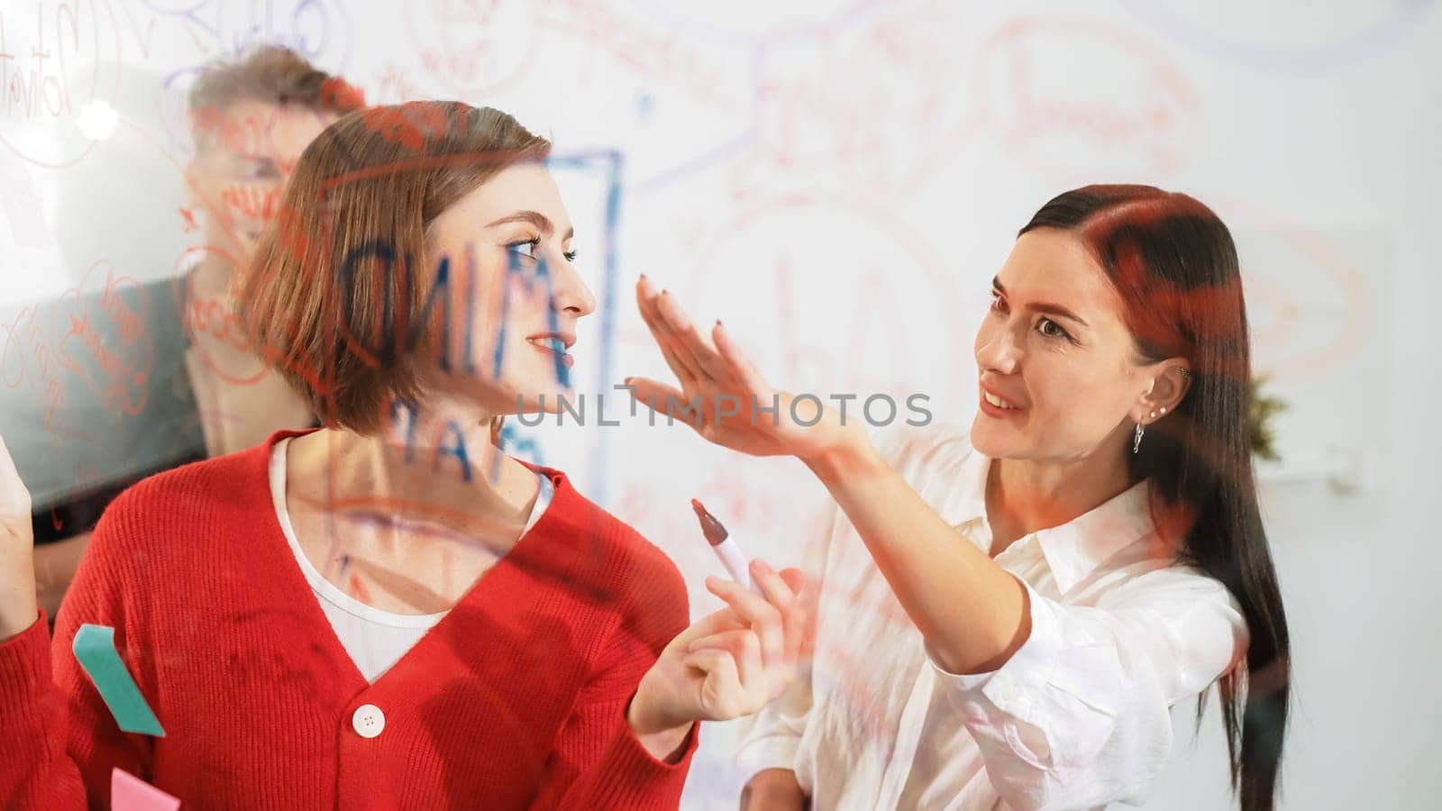 Professional business team brainstorming and working together about marketing project. Female caucasian leader writing idea on stick note while coworker present her idea confidently. Immaculate.