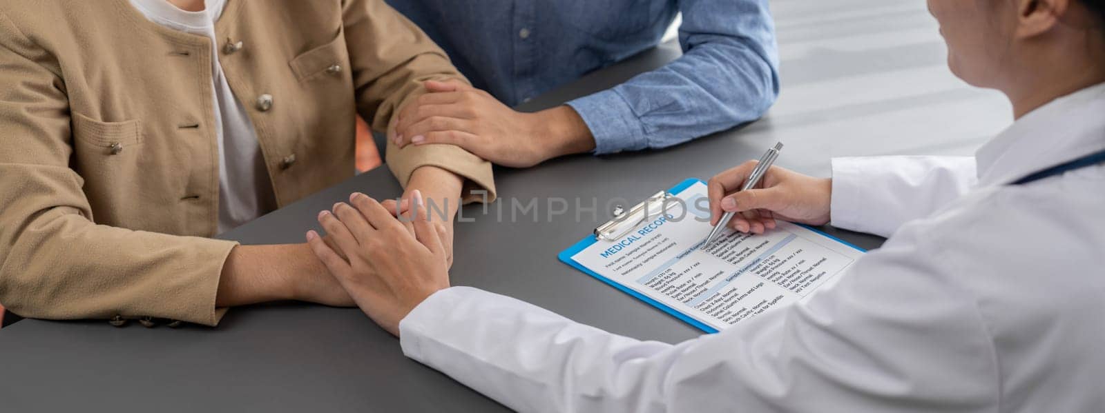 Doctor providing compassionate healthcare consultation while young couple patient holding hand, comfort each other after infertile report. Reproductive and medical fertility consulting. Neoteric