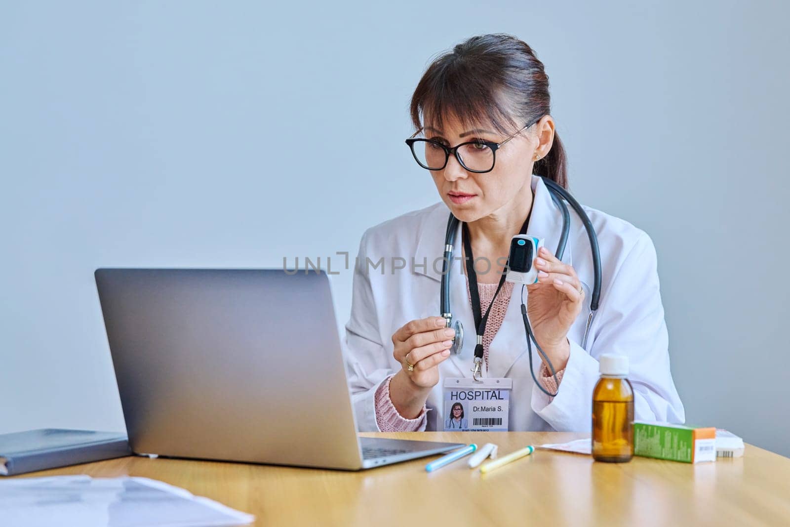 Mature woman doctor using laptop for online consultation, video call chat conference, remote meeting of medic and patient, online help, indicating recommending pulse oximeter. Health care, technology