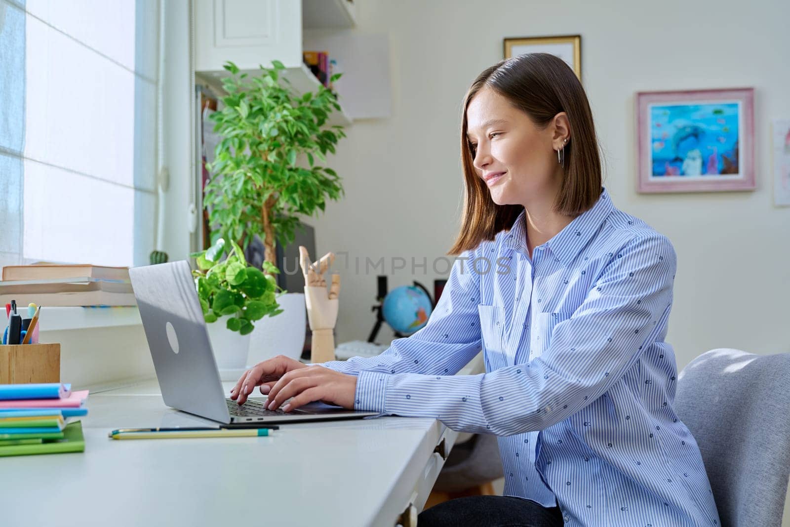 Young smiling woman typing on laptop computer at home by VH-studio