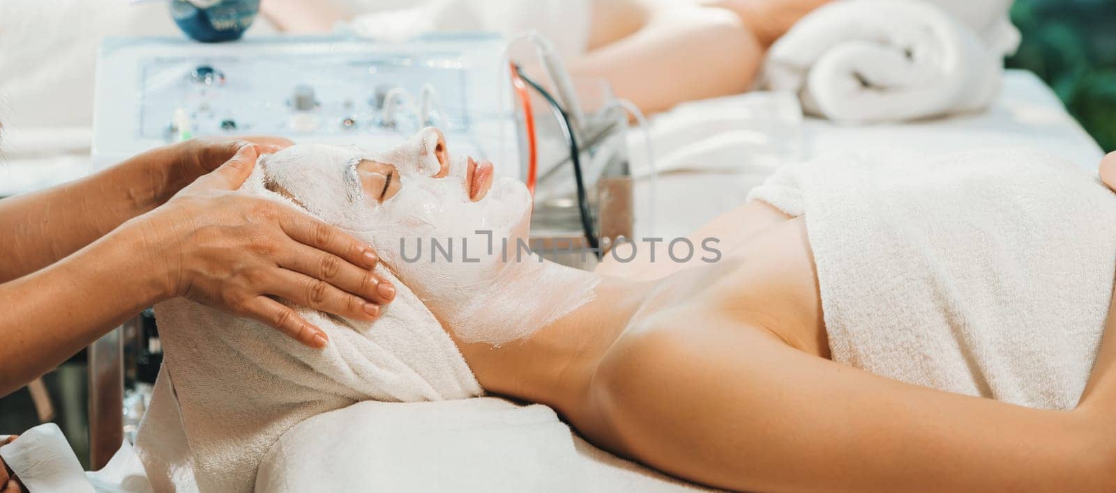 Beautiful young women lie on spa bed while having facial massage from professional doctor. Attractive female with beautiful skin surrounded by electric facial machine. Tranquility.