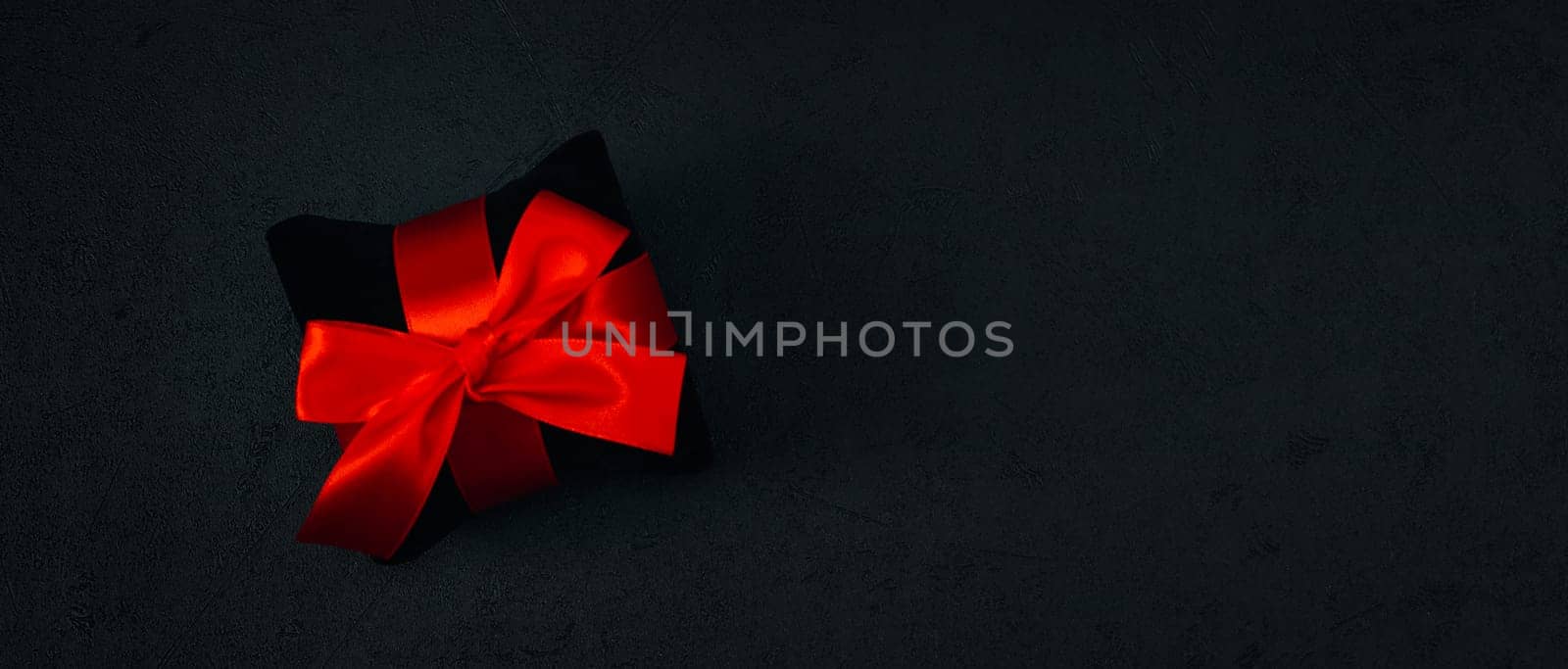 A black small velor gift pillow with a red ribbon tied in a bow by Nataliya