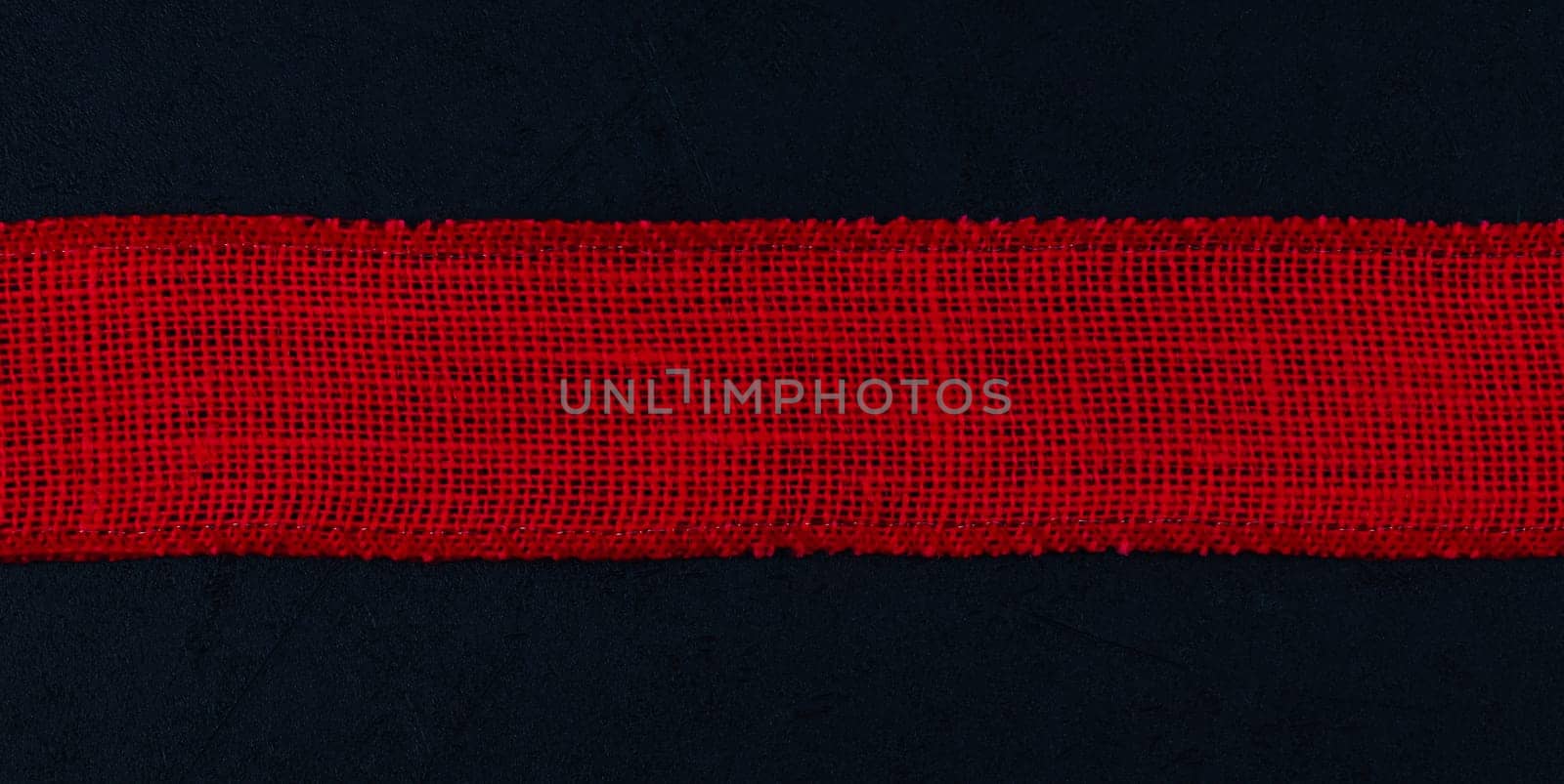 Red baggy ribbon lies in the middle on a black background with space for text on the sides, top view close-up. Concept black friday, valentine day, detective.