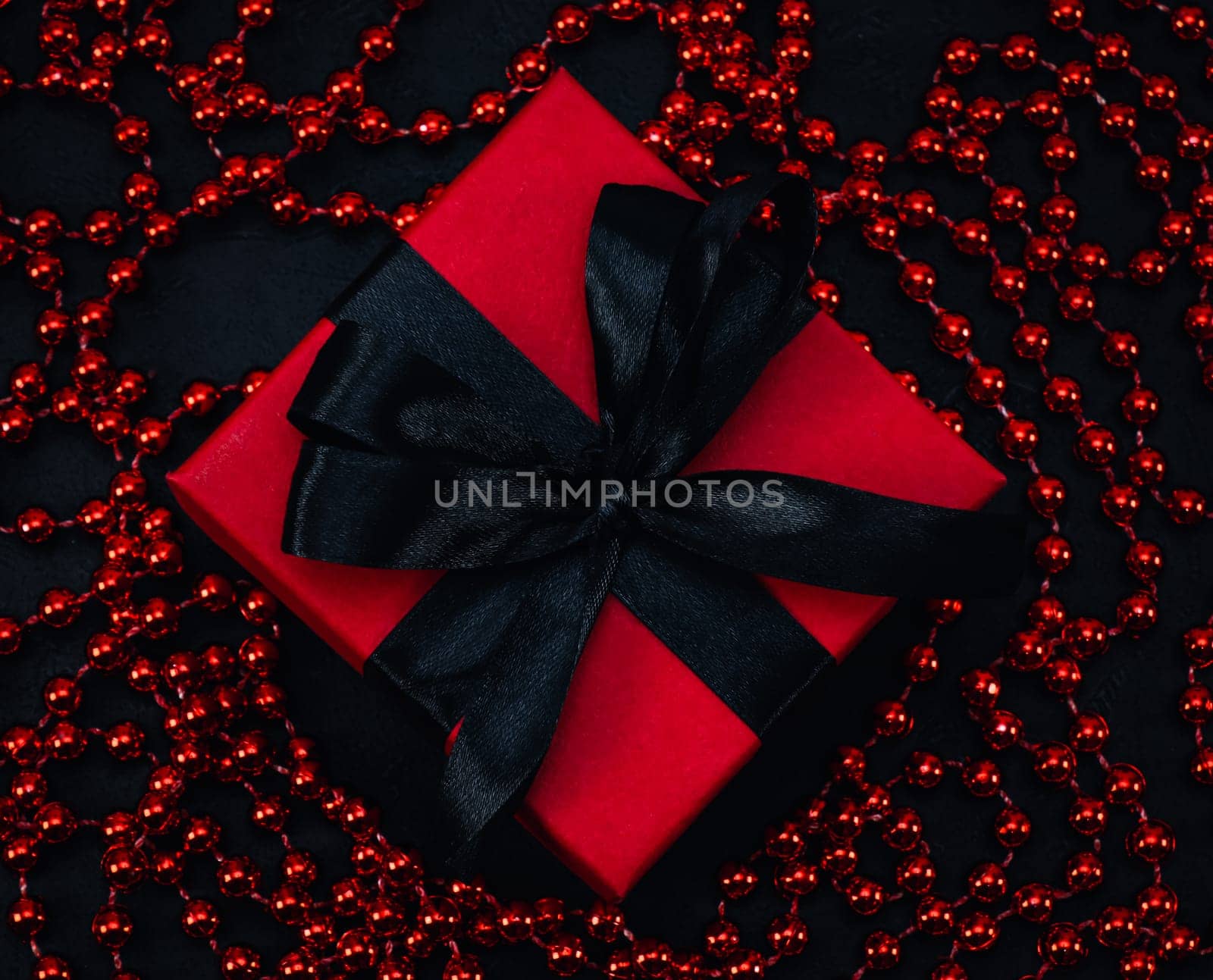 Red gift box with black ribbon and beads lie on a black background, top view close-up.Christmas and black friday concept.
