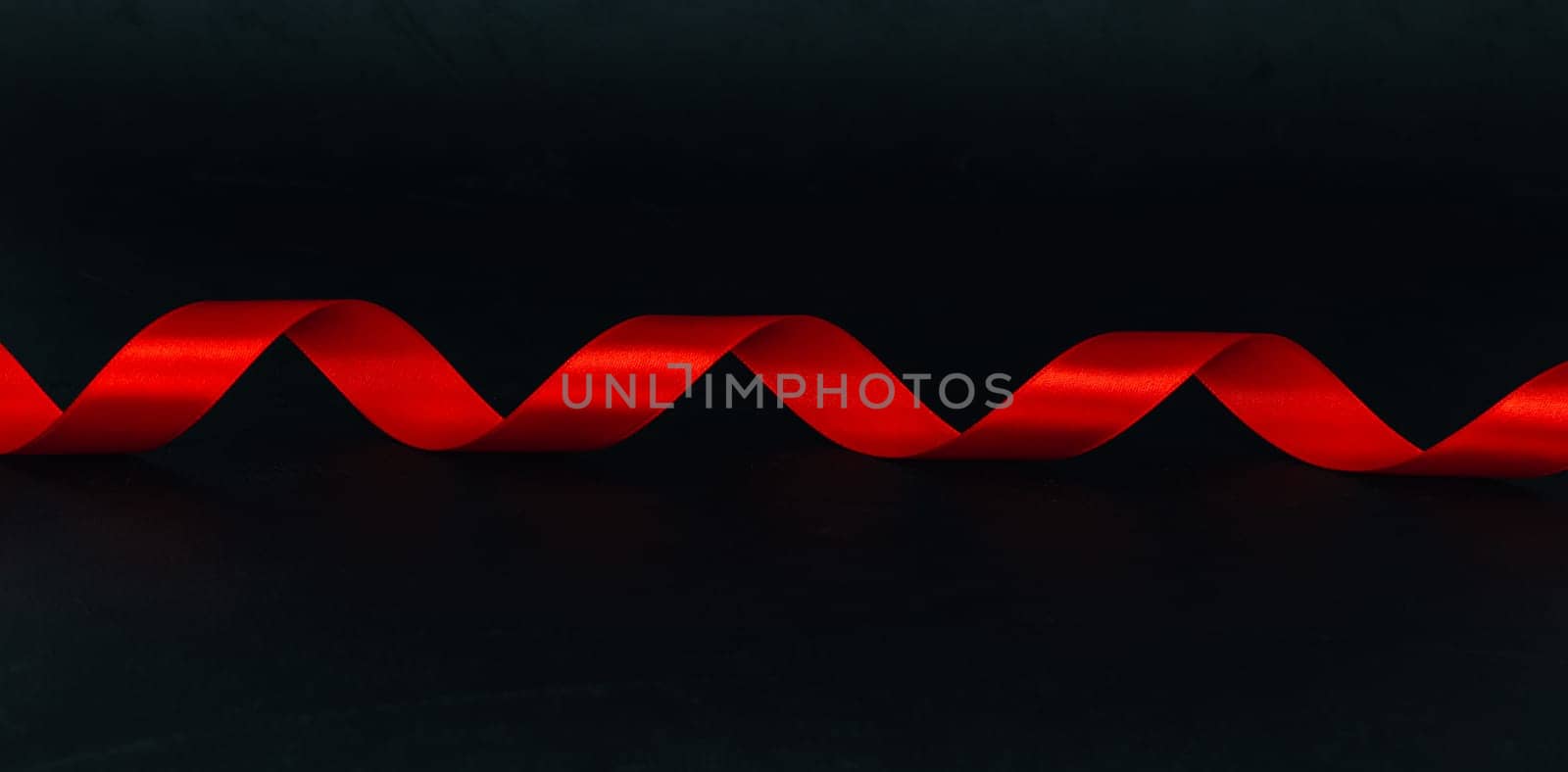 Red spiral ribbon lies in the middle on a black background with space for text on the sides, close-up side view. Concept of black friday, christmas, detective and mystic.