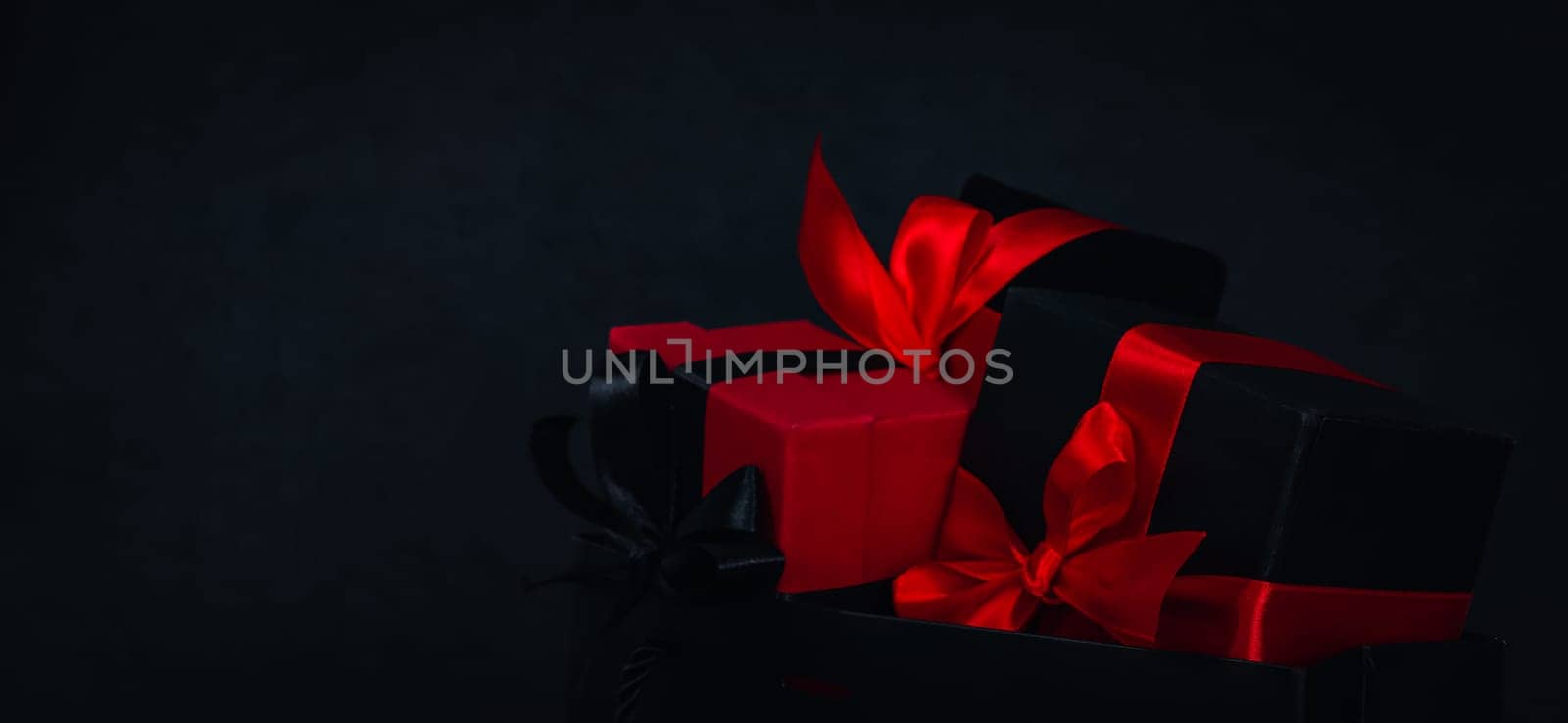 One paper bag with three gift boxes on the right against a black background with space for text on the left, close-up side view. Christmas and black friday concept.