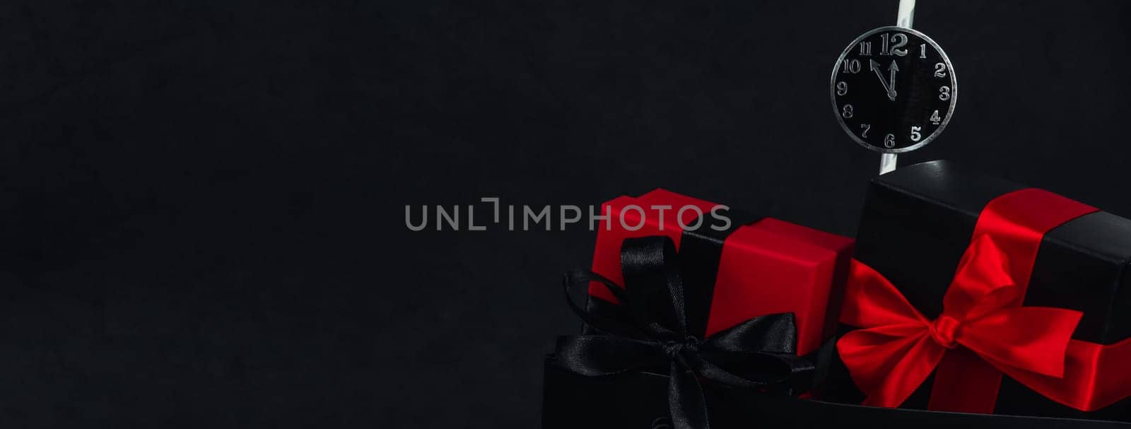 One package with two gift boxes and a paper clock on the right against a black background with space for text on the left, close-up side view. Christmas and black friday concept.