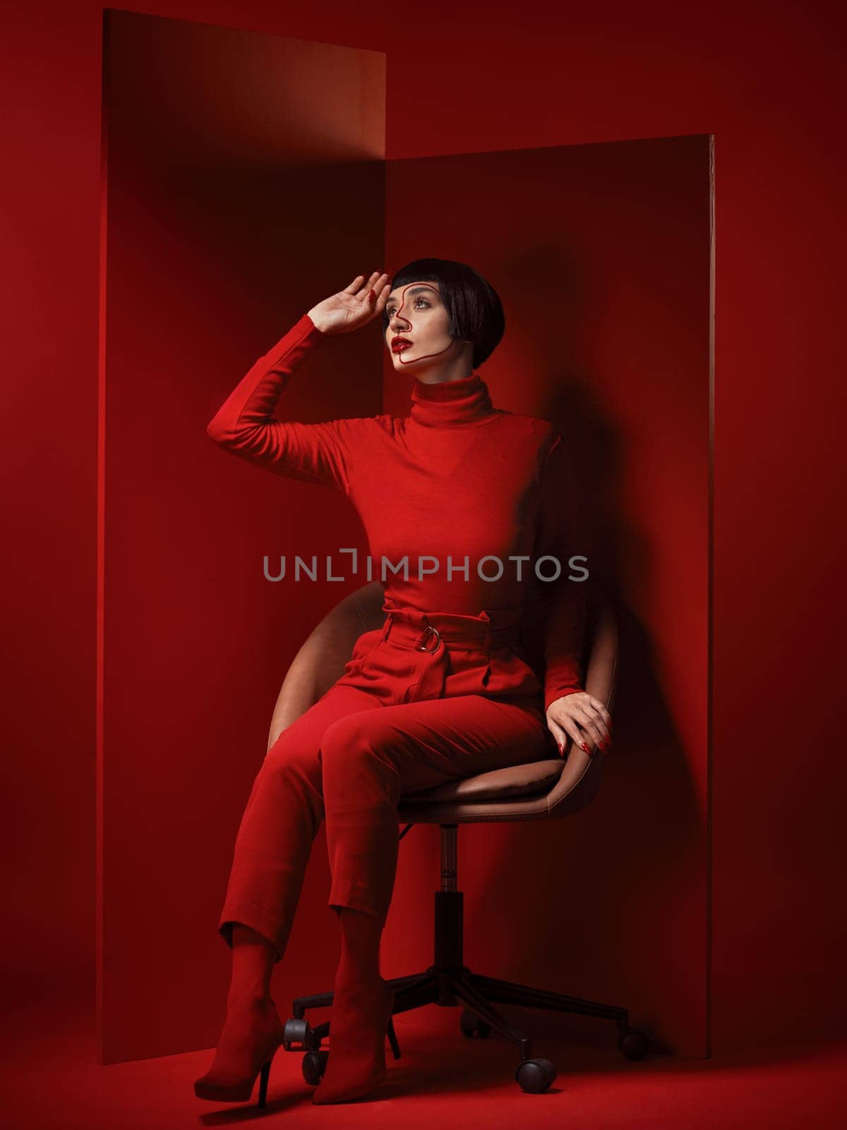 Thinking, fashion and a model woman on red background in studio for elegant, chic or trendy style. Aesthetic, art and beauty with an edgy person in unique clothes suit, makeup and cosmetics on chair.