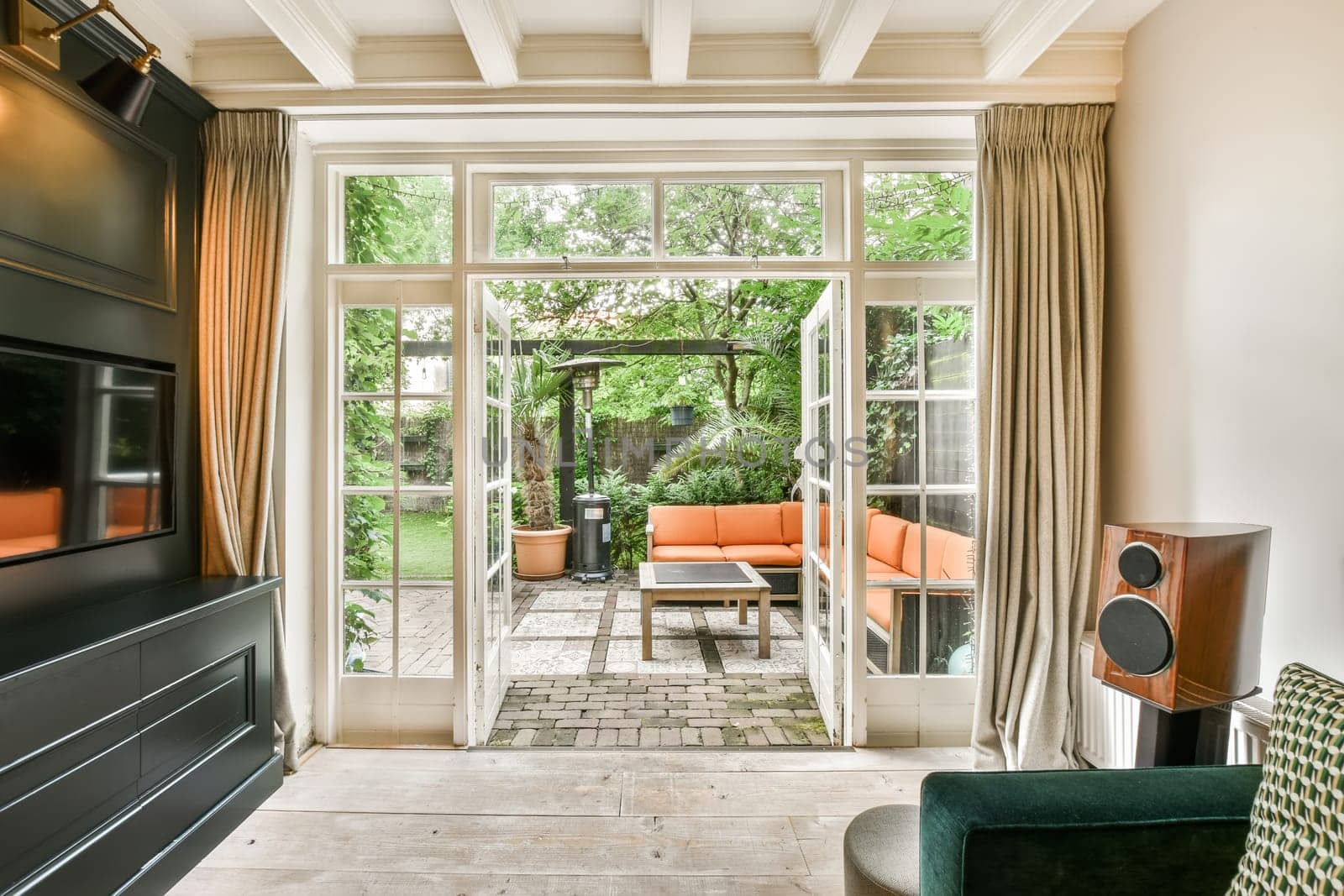 a living room with an orange couch and television set in the middle of the room, looking out to the garden