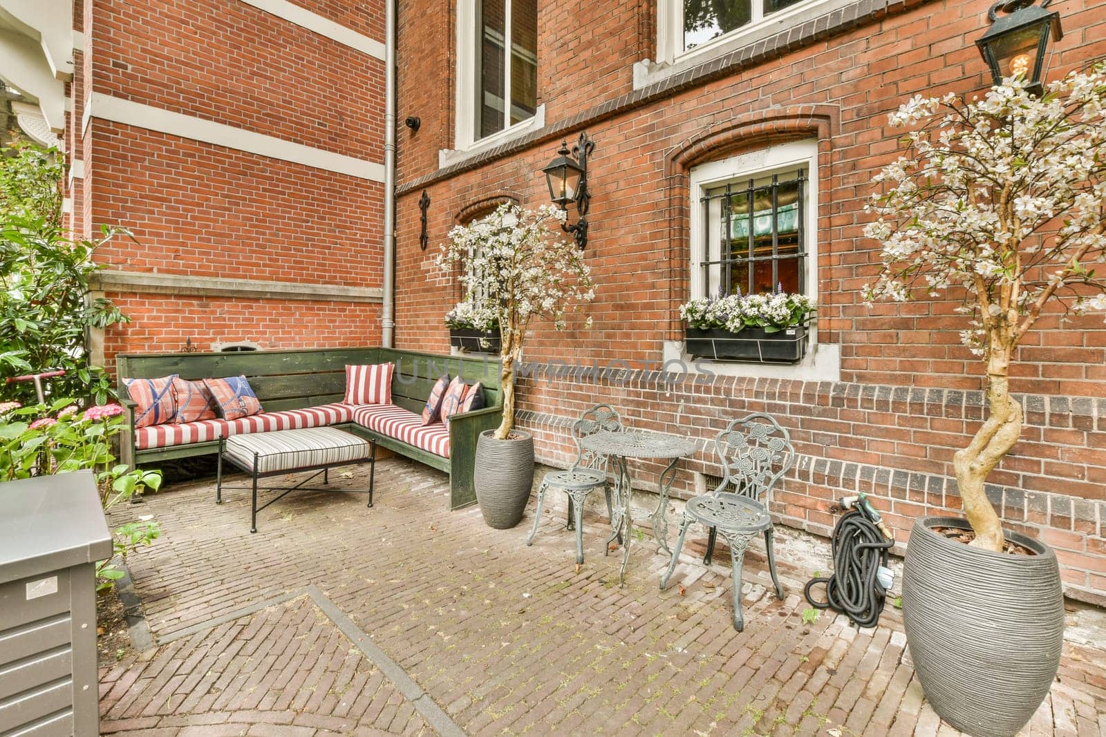 an outside area with furniture and flowers on the side of a brick building, in front of a green bench