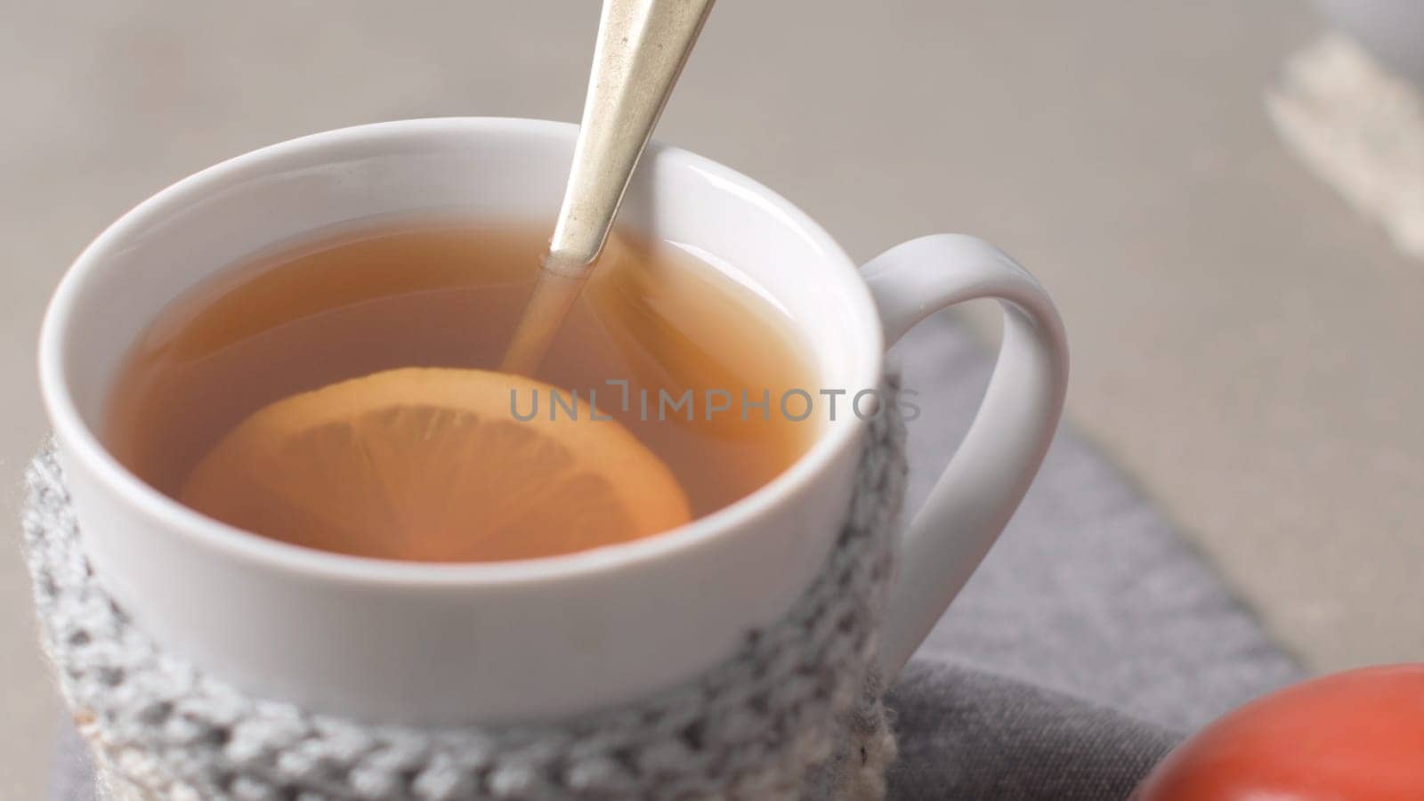 Cup of hot tea with lemon dressed in knitted warm winter scarf on wooden tabletop.