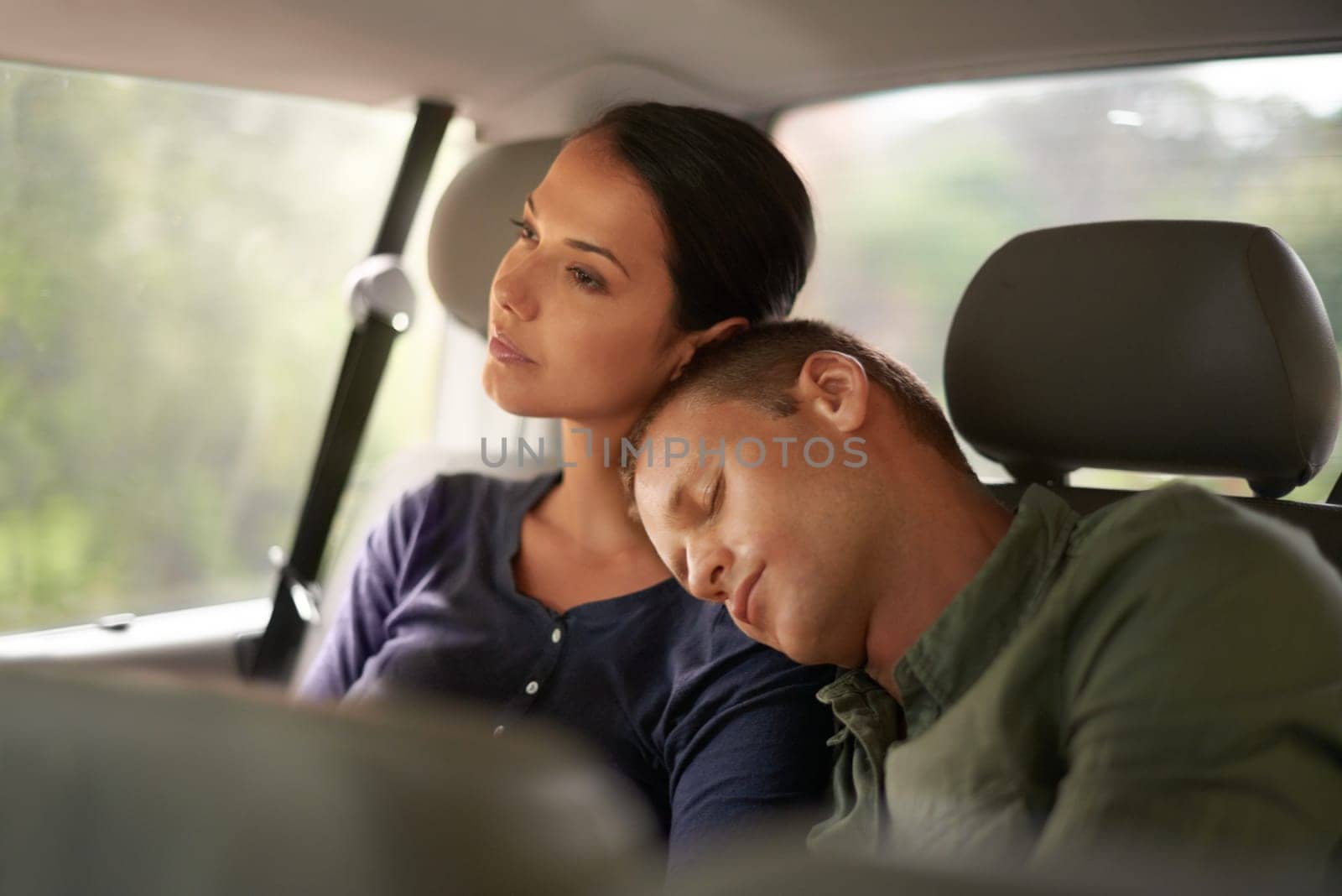 Dreaming of his next destination. An exhausted man sleeps on his wifes shoulder while they travel in a car
