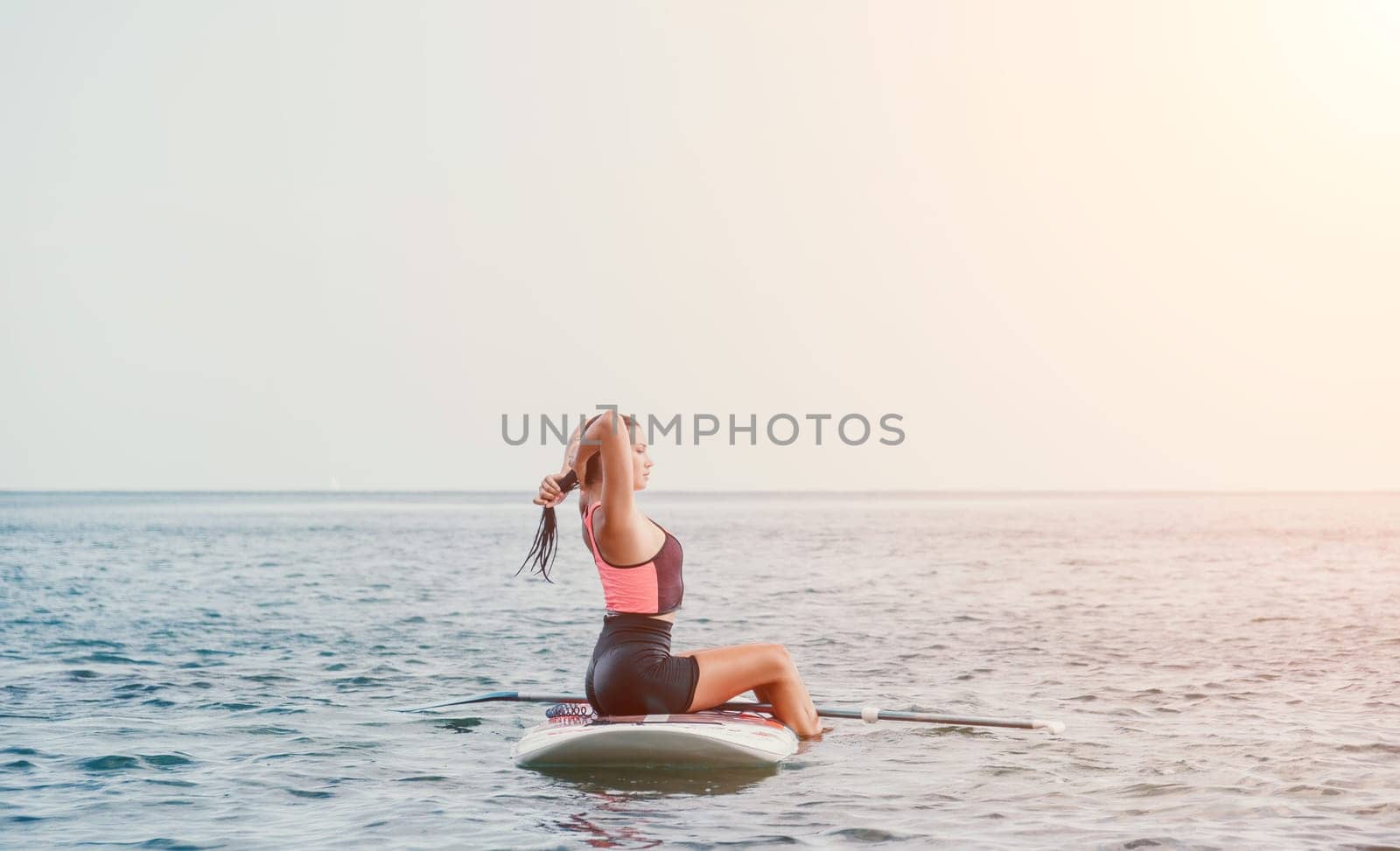 Silhouette of woman standing, surfing on SUP board, confident paddling through water surface. Idyllic sunset or sunrise. Sports active lifestyle at sea or river.