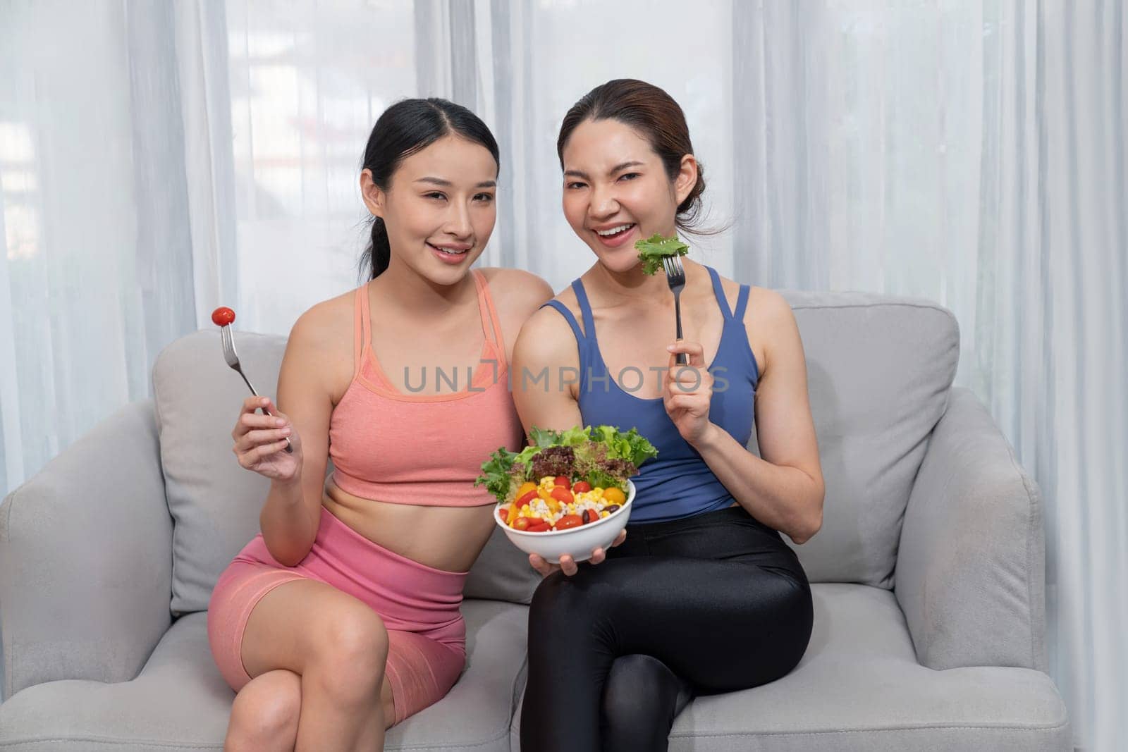 Young sporty Asian women in sportswear holding salad bowl together fill with vibrant of fruit and vegetable. Natural youthful and fit body lifestyle with balance nutrition and home exercise. Vigorous