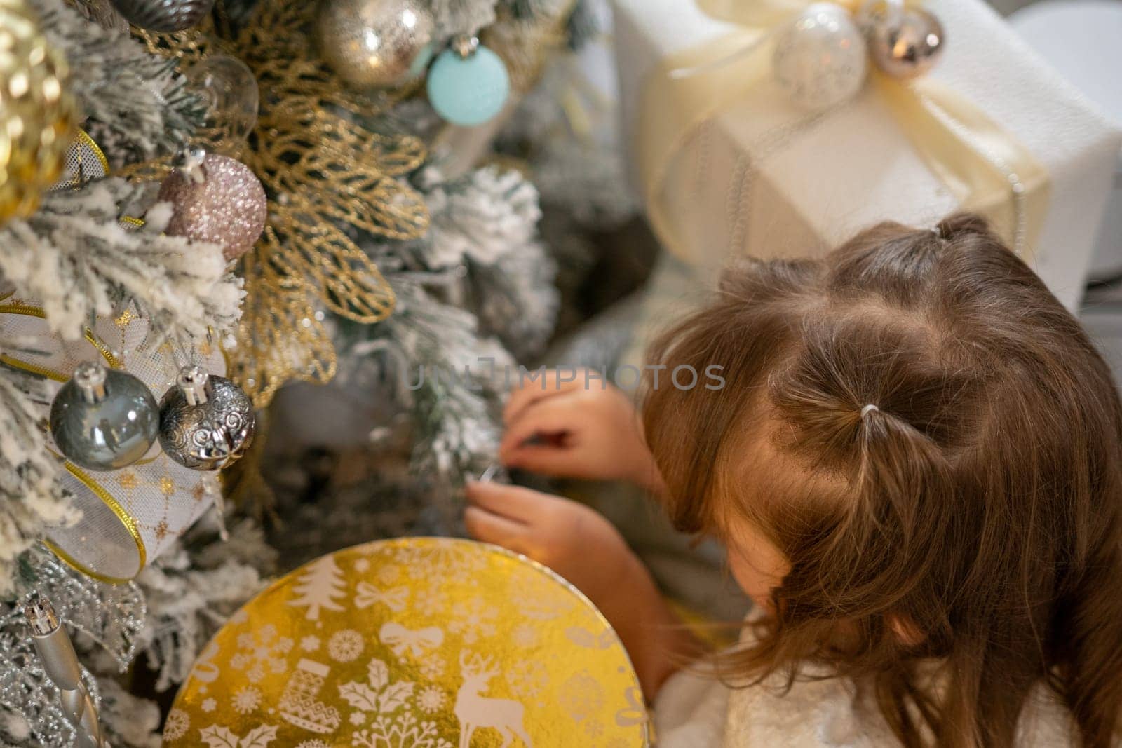 A girl in a white dress decorates a Christmas tree with her own hands, Christmas holidays at home. by Matiunina