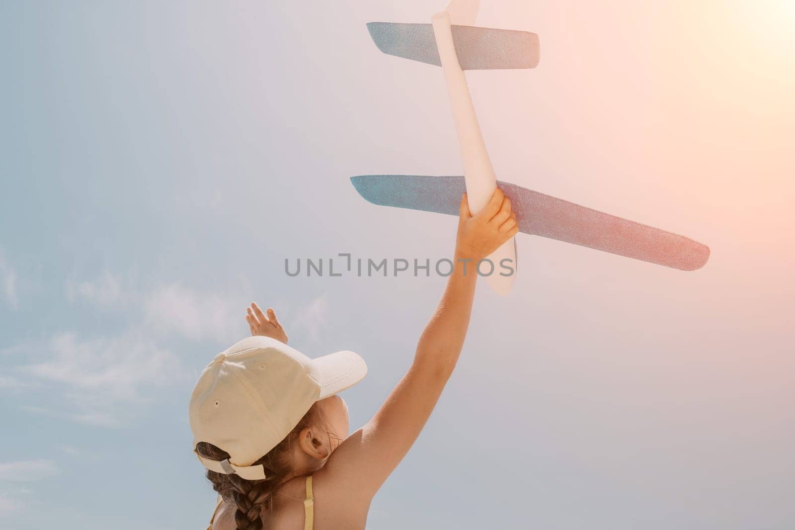 Kid playing with toy airplane. Children dream of travel by plane. Happy child girl has fun in summer vacation by sea and mountains. Outdoors activities at background of blue sky. Lifestyle moment. by panophotograph