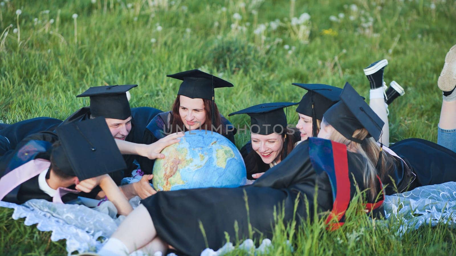 Graduate students in black robes study a globe on the grass