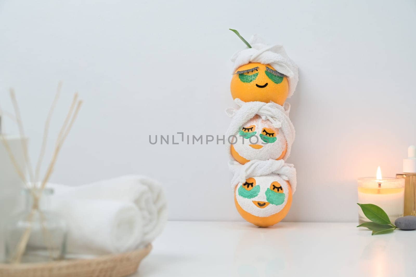 Three orange fruits in face mask near candle on white table. Spa treatment and self care concept by prathanchorruangsak