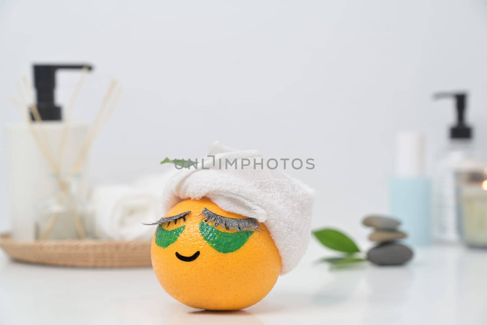 An orange fruit with towel and patches under eyes. Spa treatment and self care concept by prathanchorruangsak