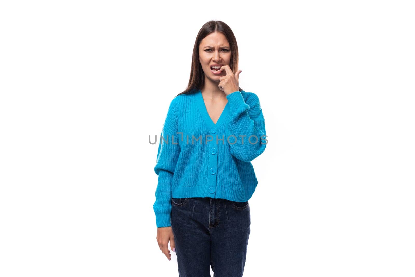 young confused caucasian woman with black hair dressed in a blue cardigan and jeans thought on a white background.