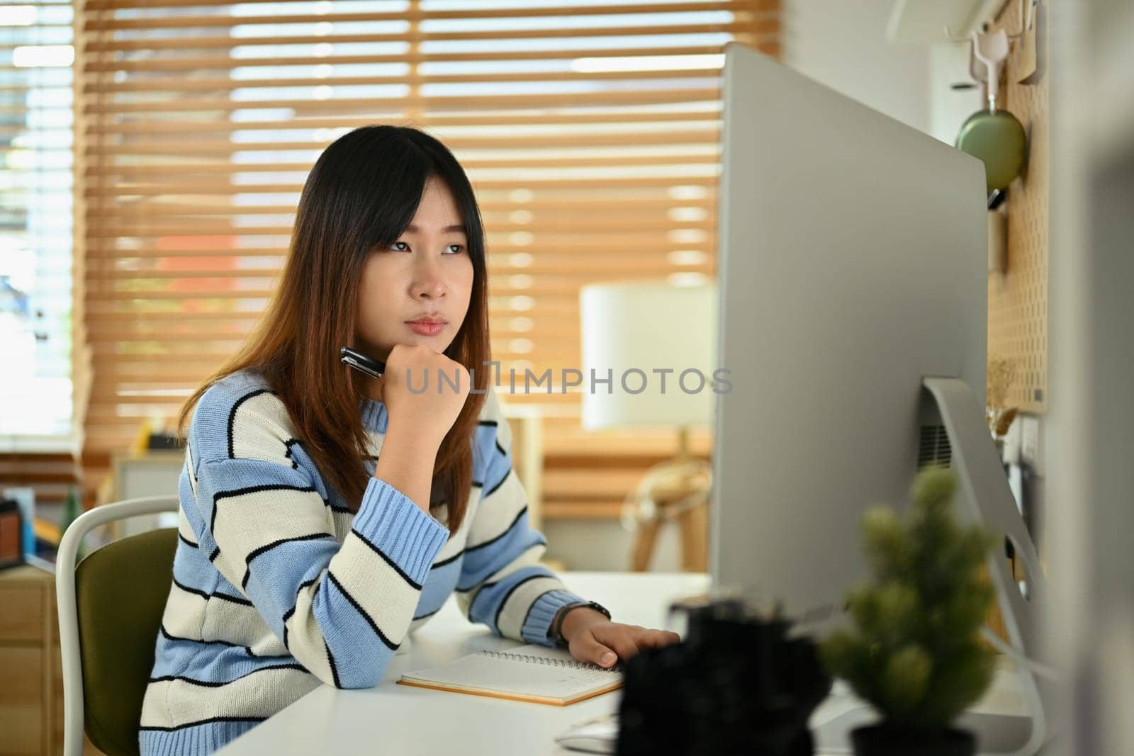 Concentrate young woman in sweater looking at computer monitor while working in cozy home.
