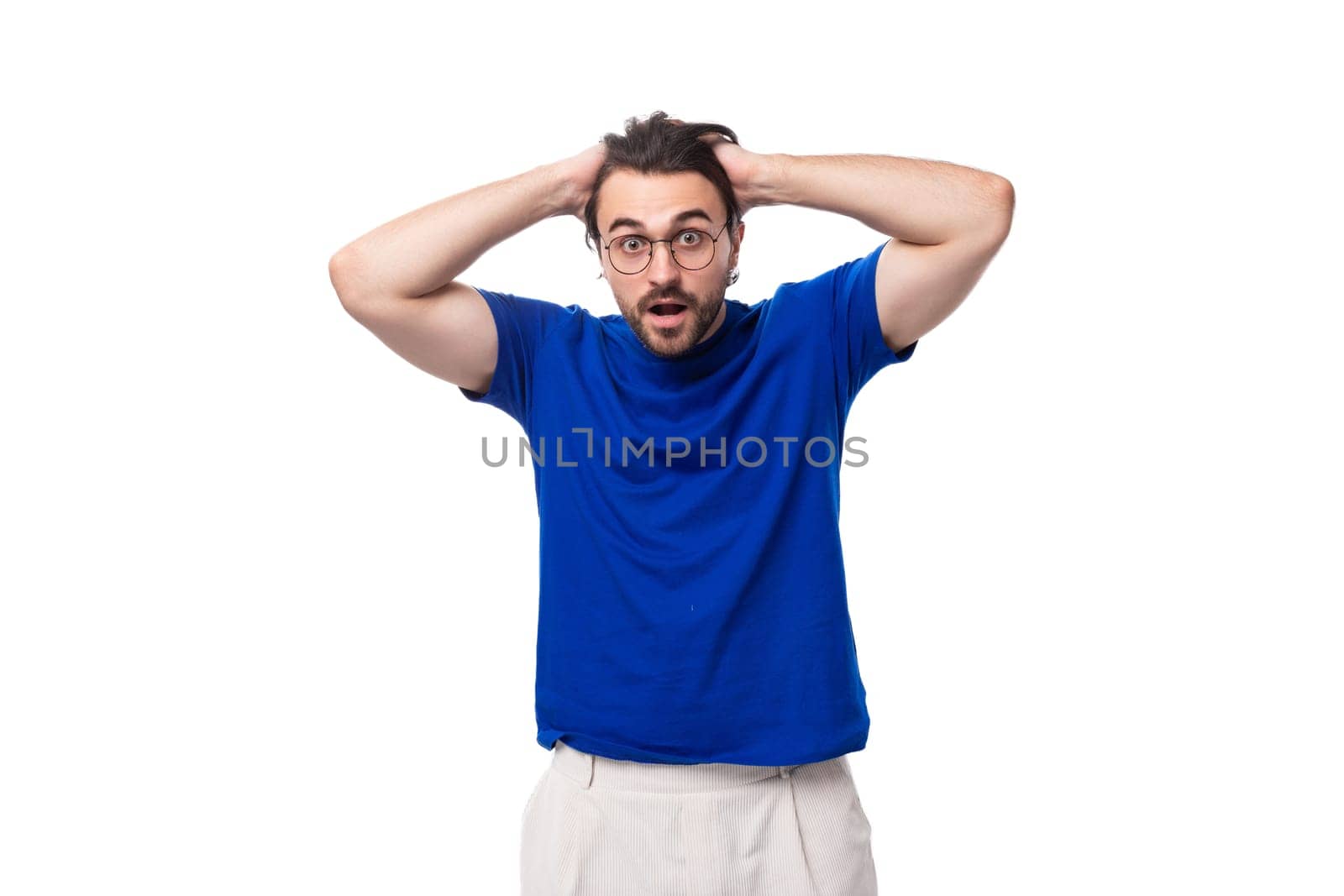 young surprised european brunette man with a beard in glasses dressed in a blue t-shirt.