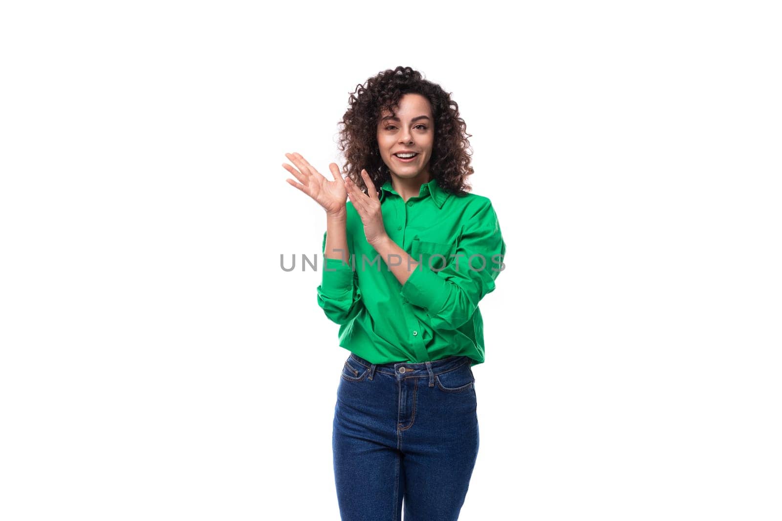 young stylish caucasian brunette woman with curled hair dressed in a green shirt posing on a white background with copy space.