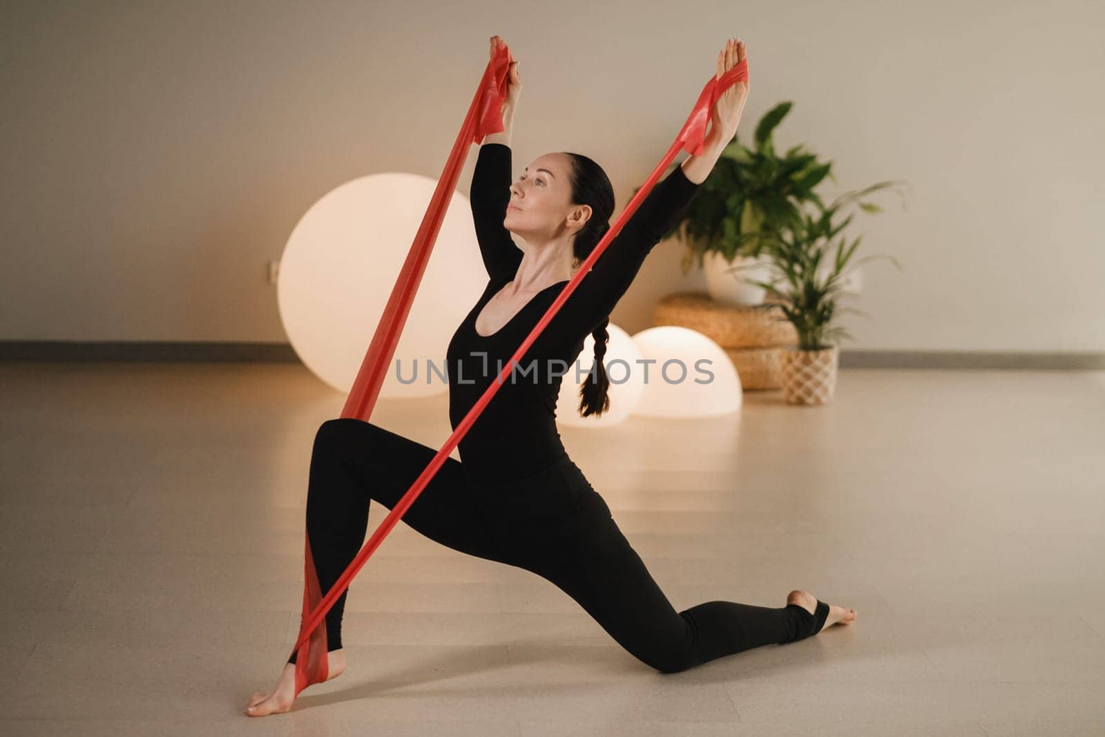 Girl in black doing fitness with red ribbons indoors by Lobachad