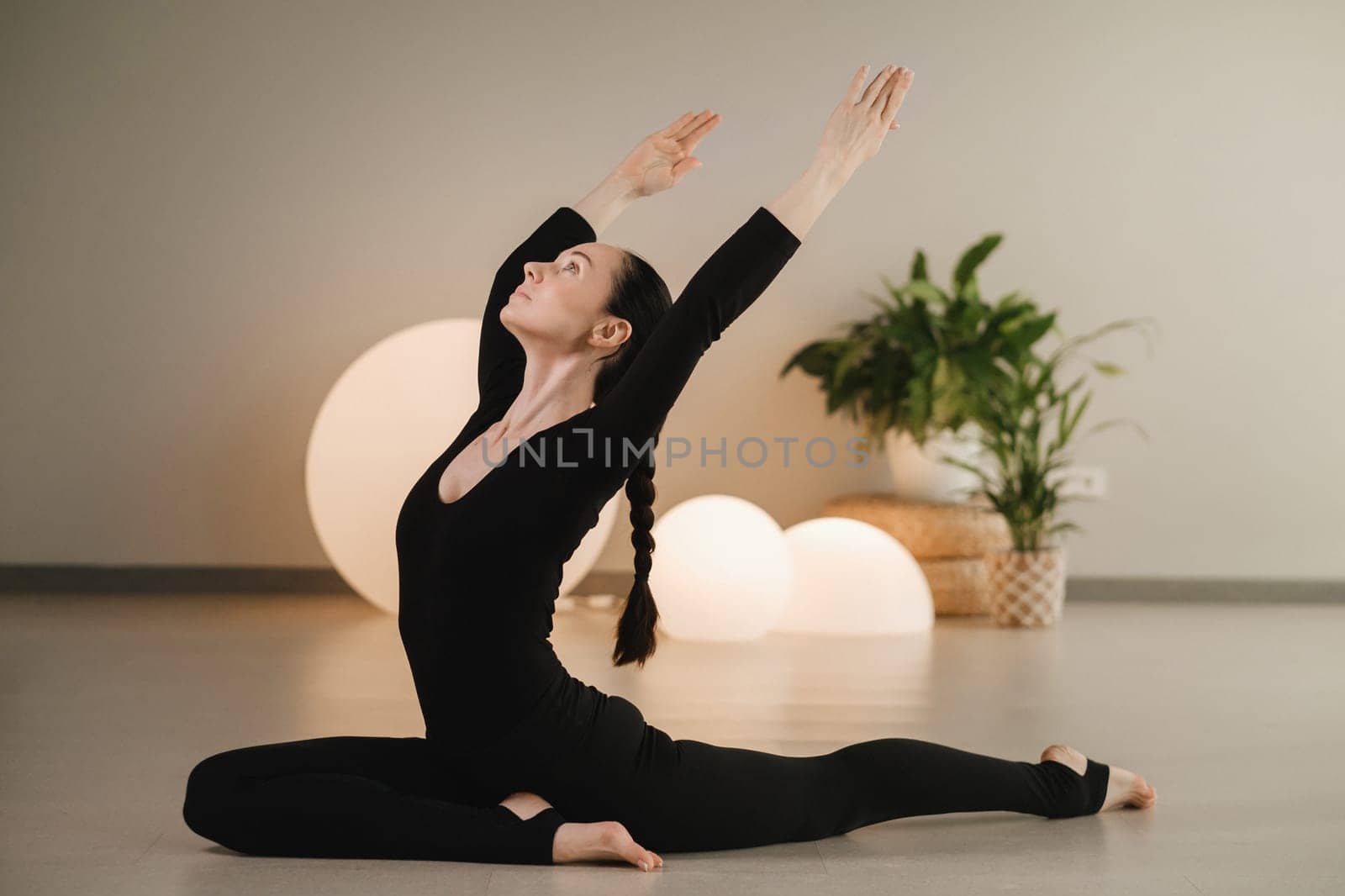 A girl in black clothes does yoga on a mat indoors.