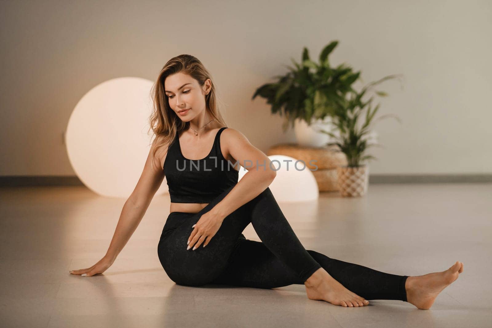 A girl in black clothes does yoga on a mat indoors.