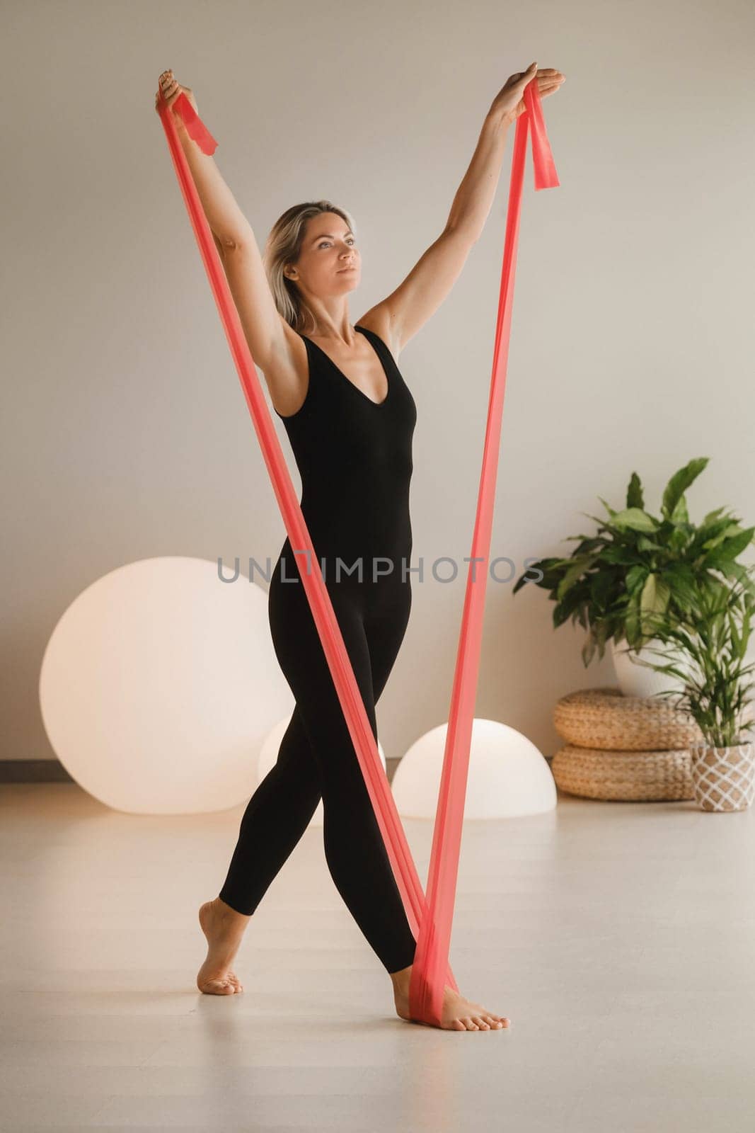 Girl in black doing fitness with red ribbons indoors by Lobachad