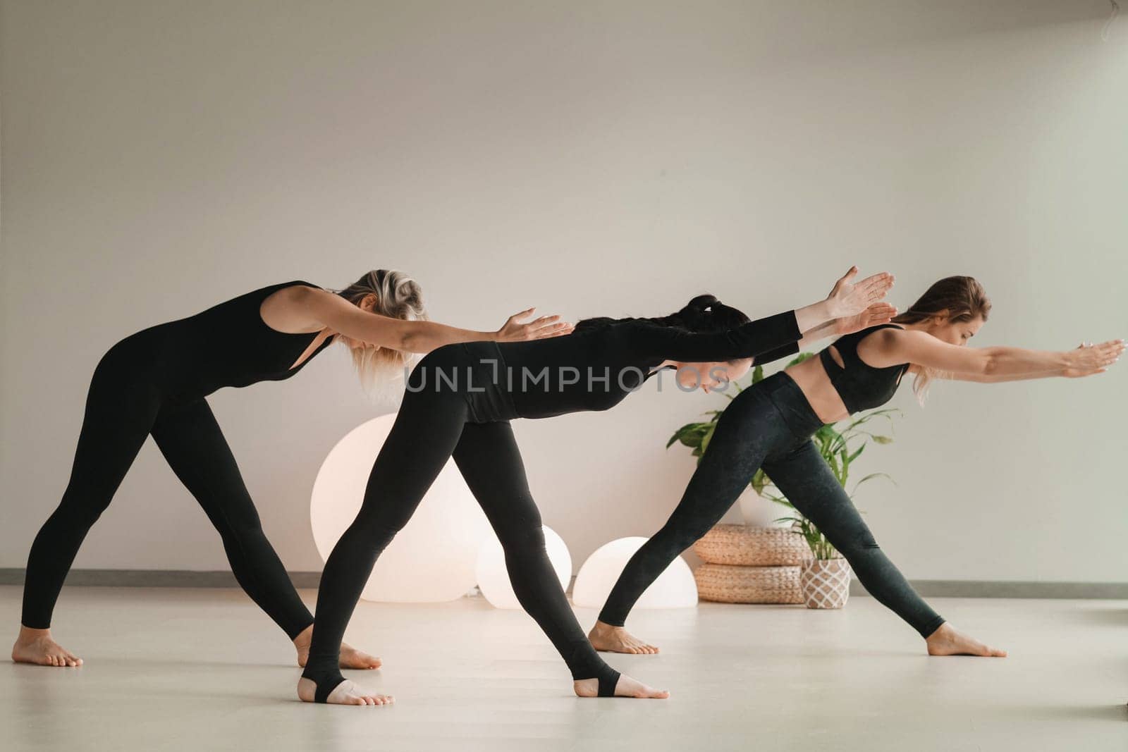 A group of girls in black doing yoga poses indoors. Women are engaged in fitness by Lobachad