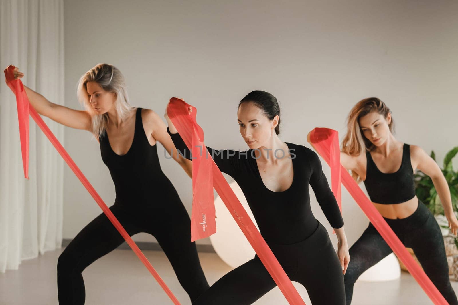 Girls in black are doing fitness with red ribbons indoors.
