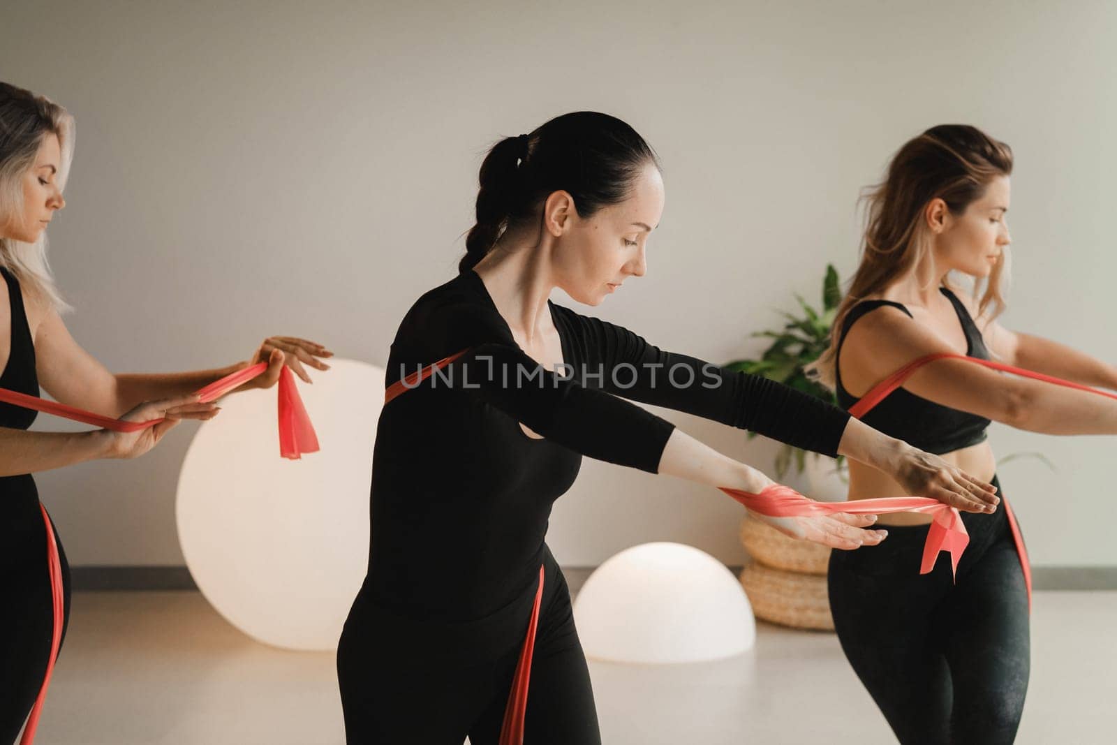 Girls in black are doing fitness with red ribbons indoors.