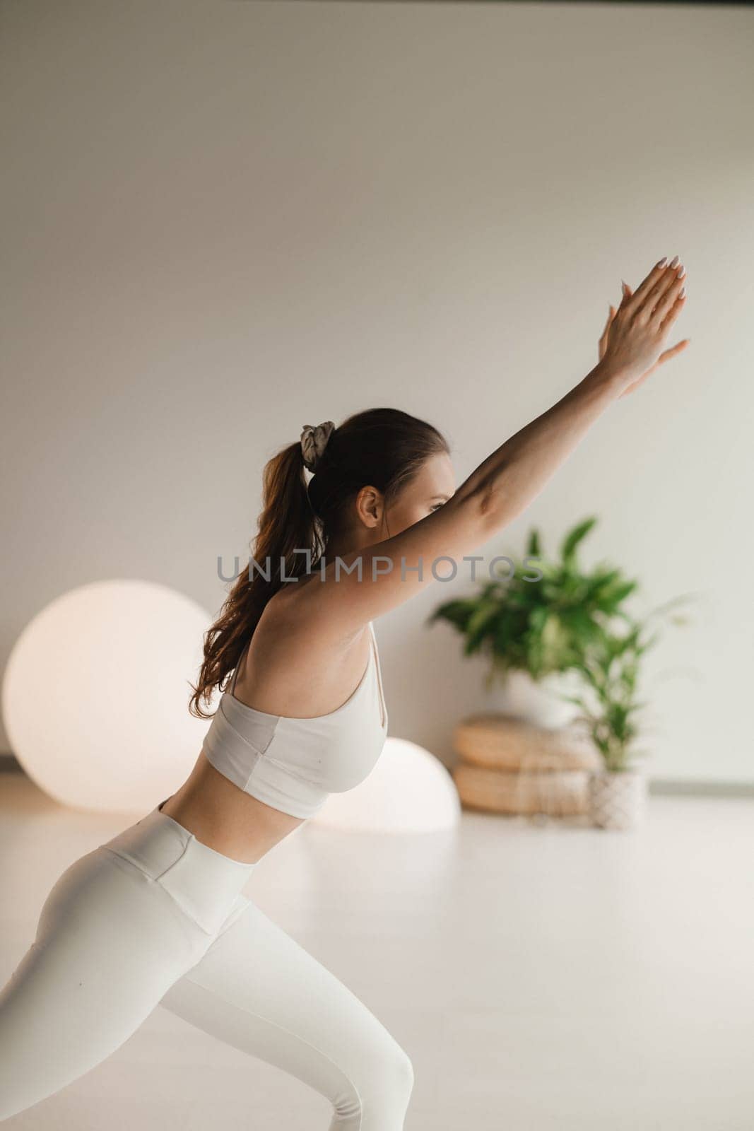 A girl in white clothes does yoga on a mat indoors.