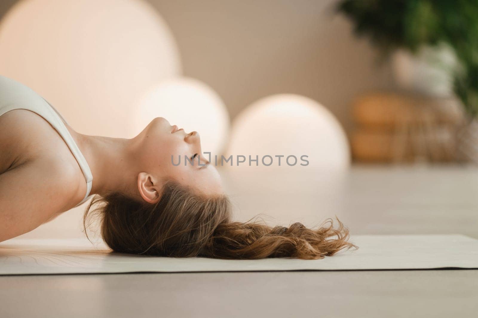 A girl in white clothes does yoga lying on a rug indoors.