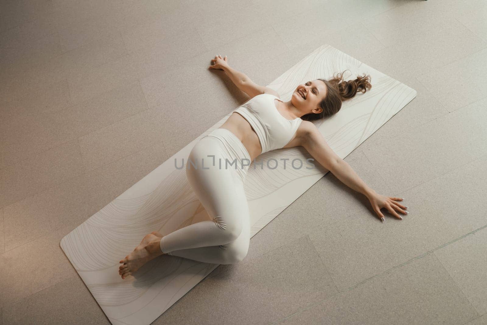 A girl in white clothes does yoga lying on a rug indoors by Lobachad