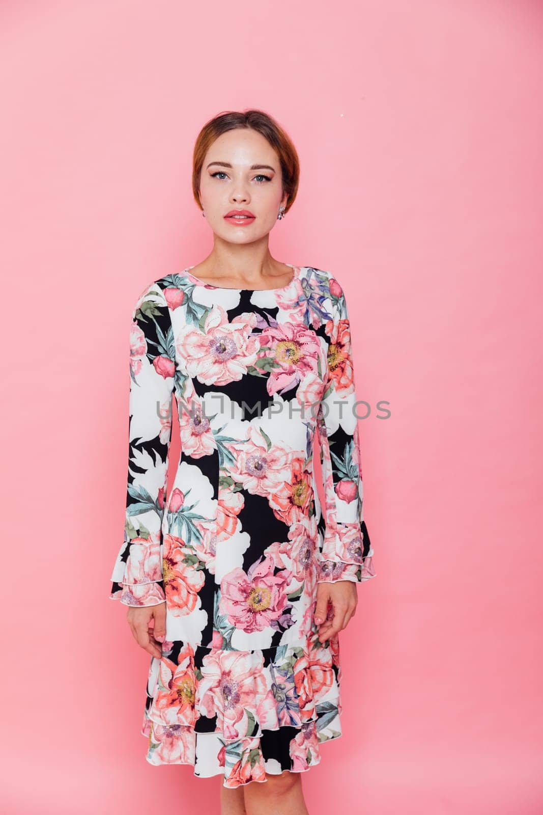 beautiful woman in a floral dress poses on a pink background
