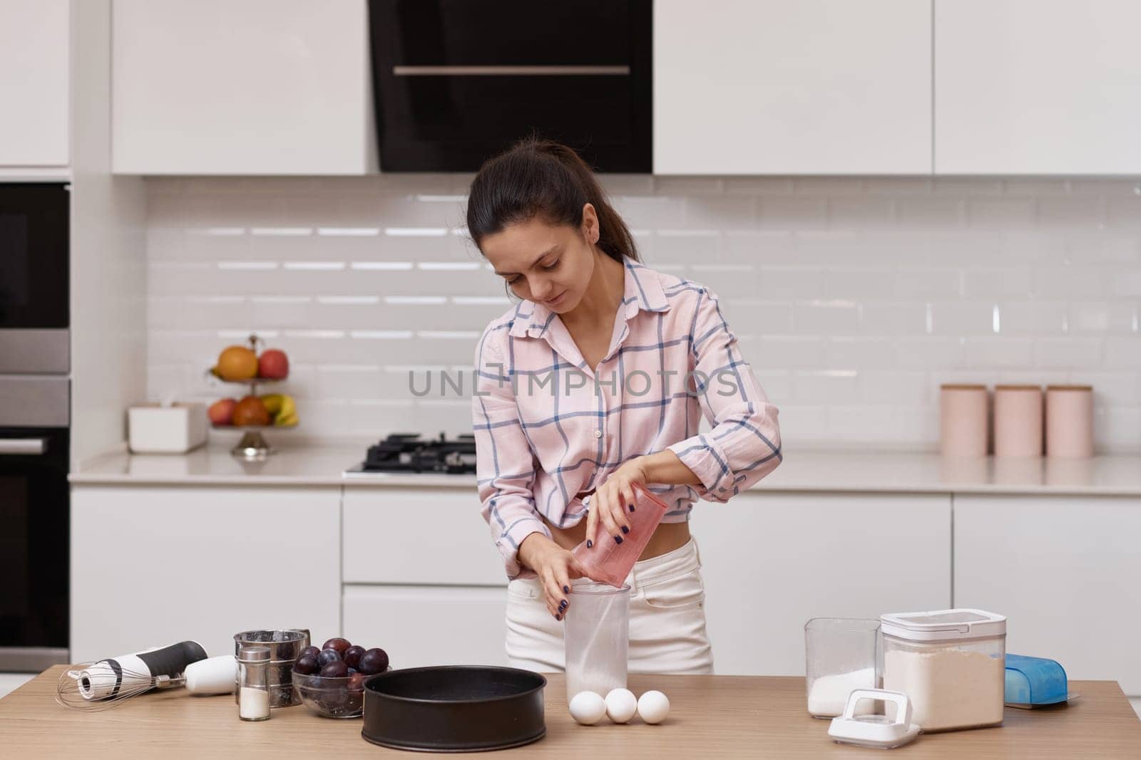 Happy housewife woman preparing pie, adding ingredients to bowl in modern kitchen